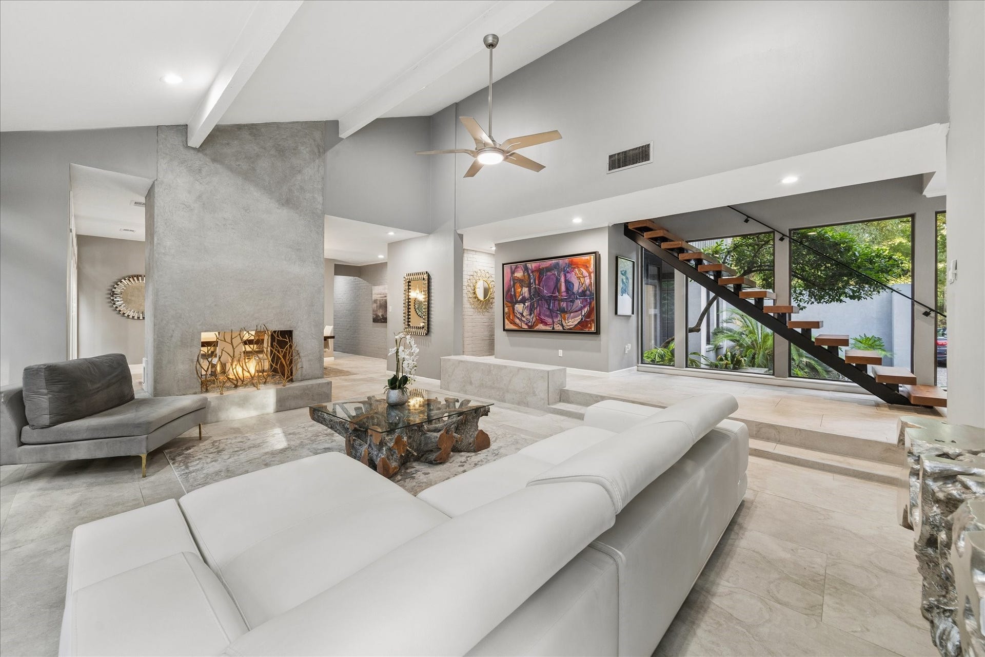 2411 Oakbank Drive, Kingwood, TX 77339 This spacious, modern living room features high ceilings, a sleek, open staircase, and large windows offering abundant natural light. The contemporary design includes a textured fireplace, elegant gray and white tones, and stylish furnishings, creating a welcoming and sophisticated atmosphere.