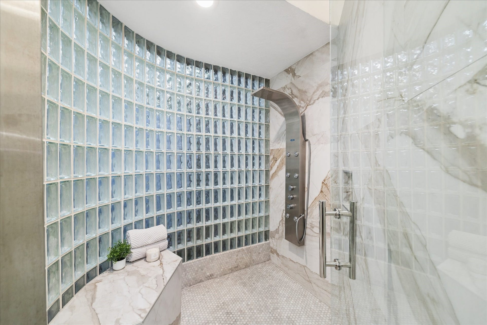 2411 Oakbank Drive, Kingwood, TX 77339 The primary bathroom features a spacious glass block shower with elegant marble walls and floors. It includes a sleek shower panel with multiple settings, complemented by a built-in marble bench for added comfort and luxury.