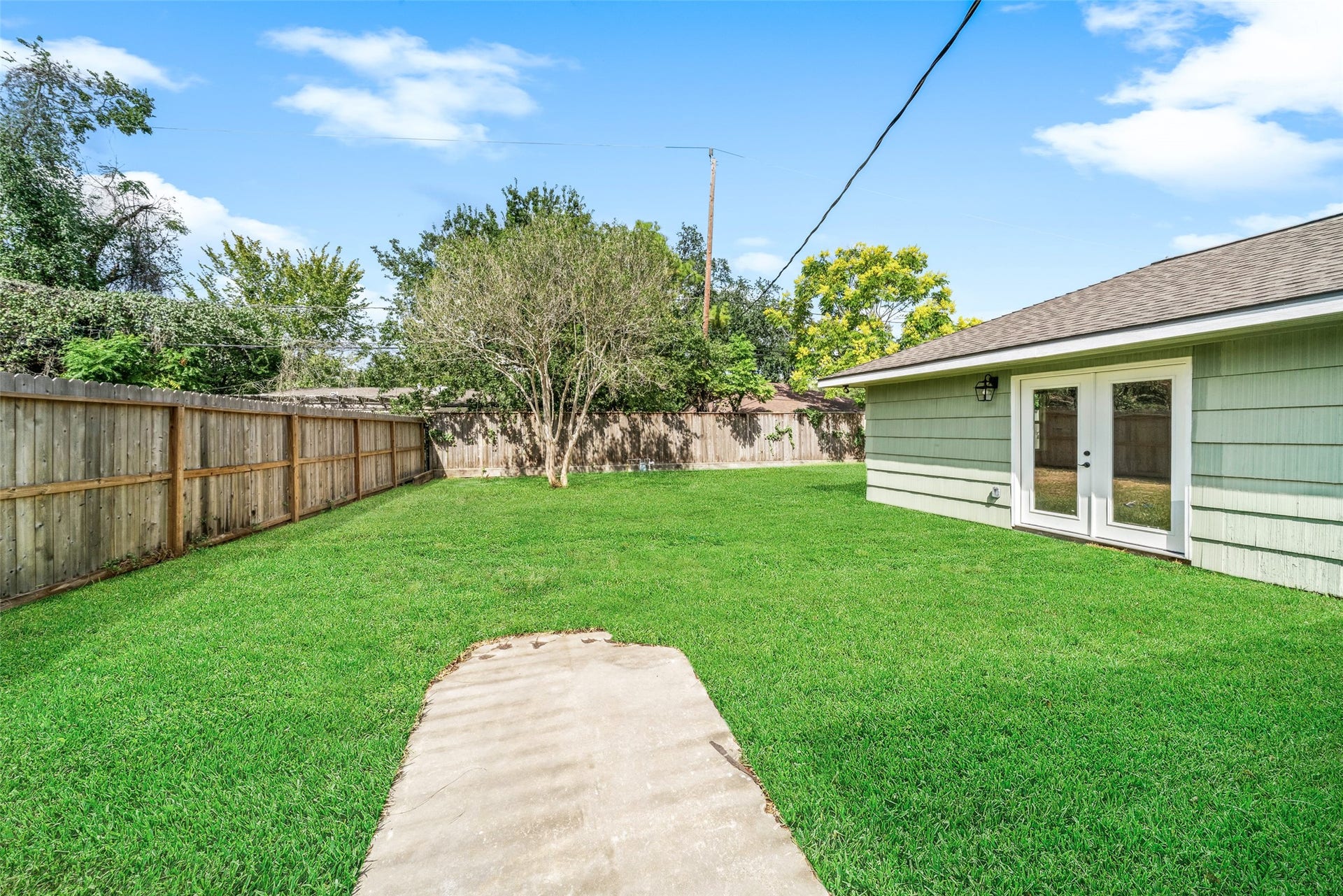 4806 Hummingbird Street, Houston, TX 77035 Spacious backyard with lush green lawn, a charming tree, and a private wooden fence, complemented by inviting French doors leading to the home.