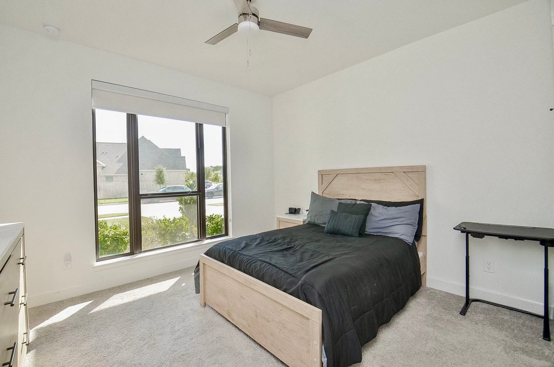 Bright secondary bedroom downstairs with large windows for natural light, and ceiling fan.