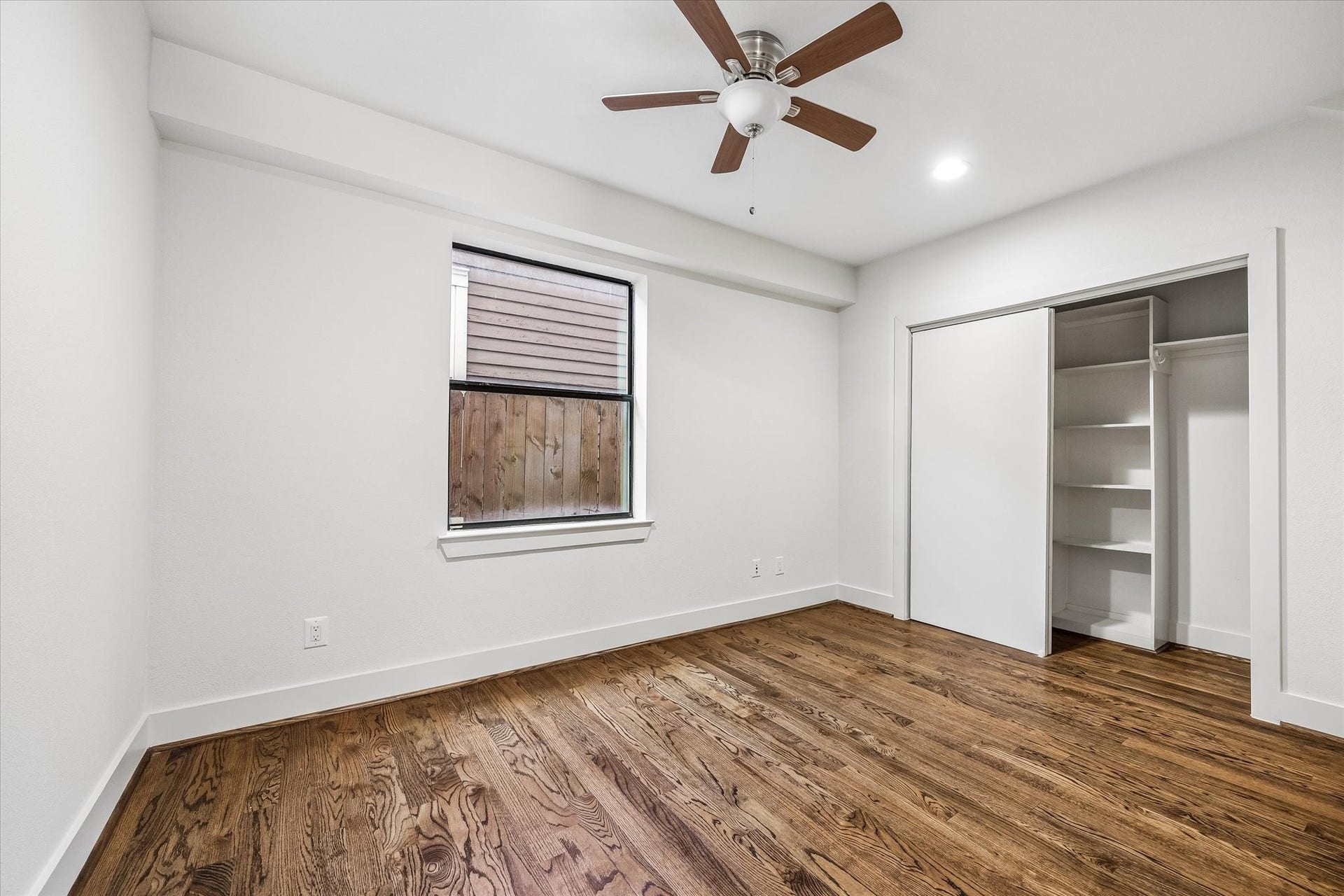 1215 Summer Street, #A, Houston, TX 77007 First floor bedroom with wood flooring, a ceiling fan, and a window for natural light. A wide closet includes built-in shelving and hanging space behind sliding doors.