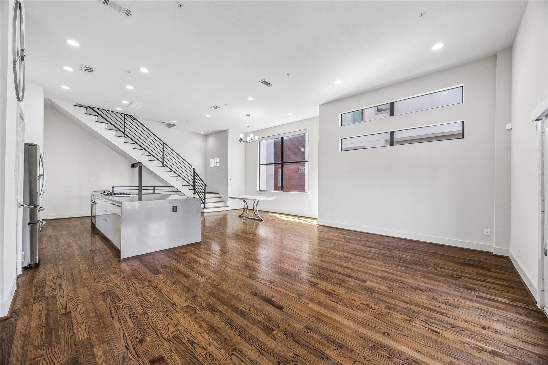 1215 Summer Street, #A, Houston, TX 77007 Open living, dining, and kitchen areas offer a connected layout with abundant natural light, continuous wood flooring, and a staircase with horizontal metal railings.