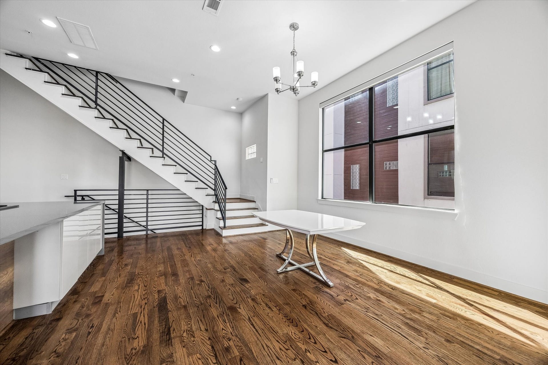 1215 Summer Street, #A, Houston, TX 77007 Bright dining area beside an oversized window, with wood flooring and an open connection to the kitchen. The adjacent staircase features wood treads and horizontal metal railings.