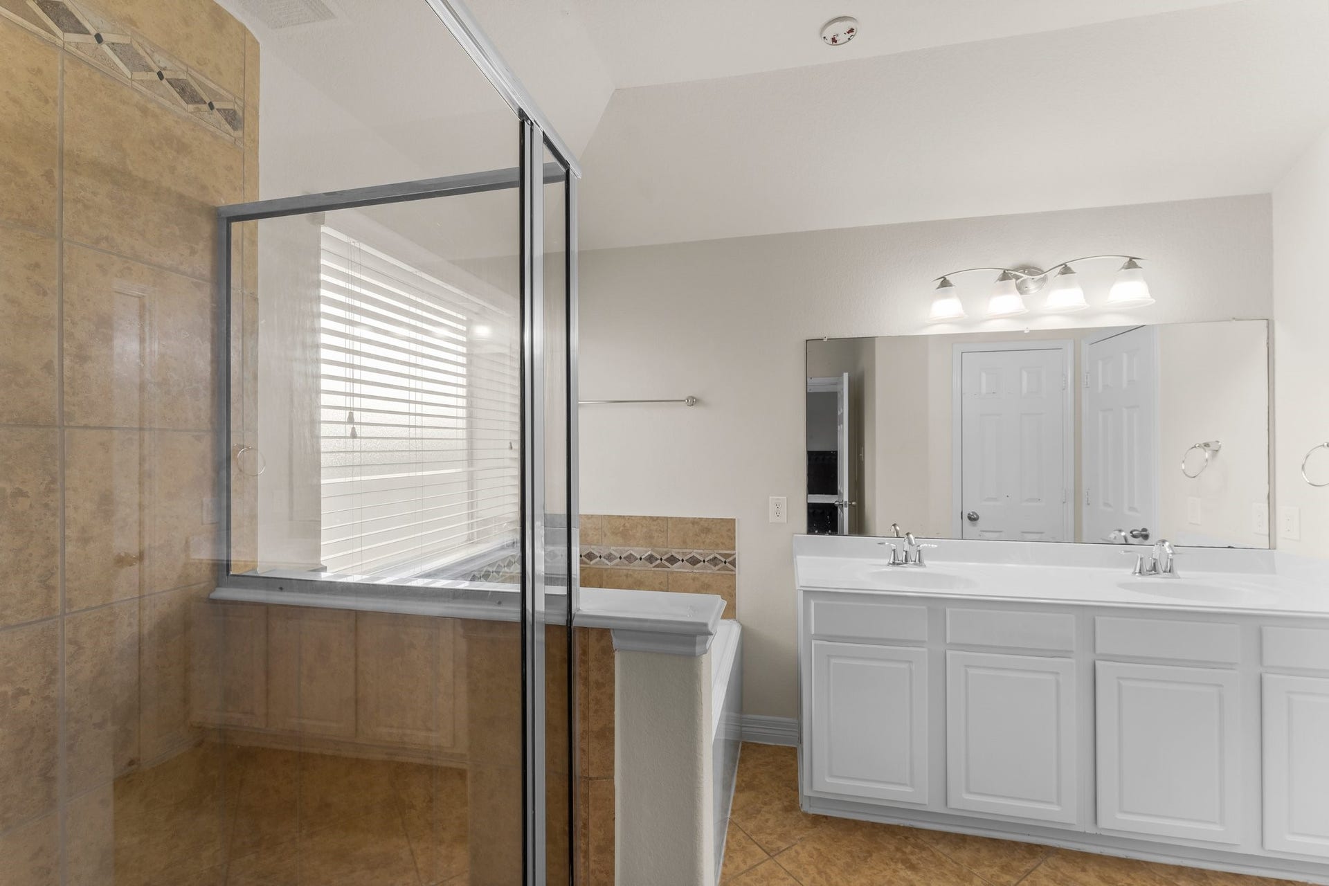 Spacious bathroom featuring a glass-enclosed shower, double vanity with sleek fixtures.
