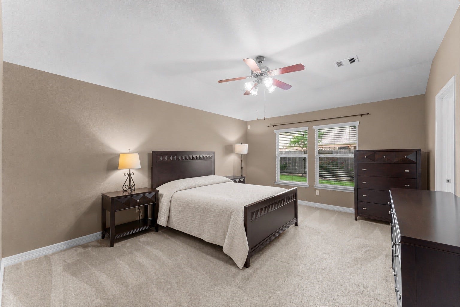 Primary bedroom with abundant natural light from two large windows overlooking the backyard.