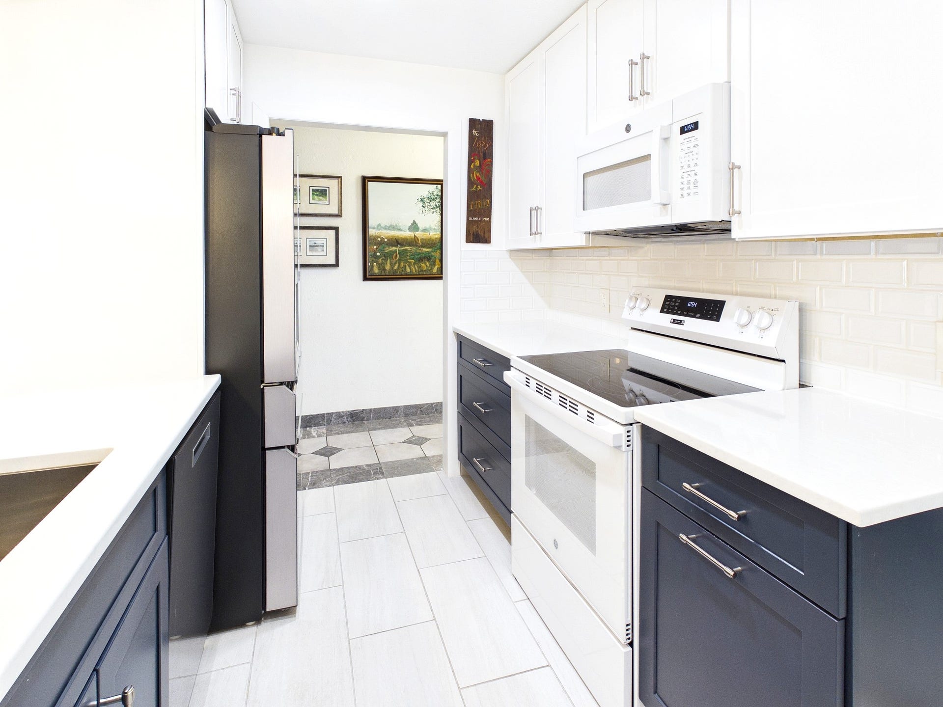 Modern kitchen with sleek white cabinetry, dark lower cabinets, and stainless steel appliances, offering a bright and inviting space for culinary enthusiasts.