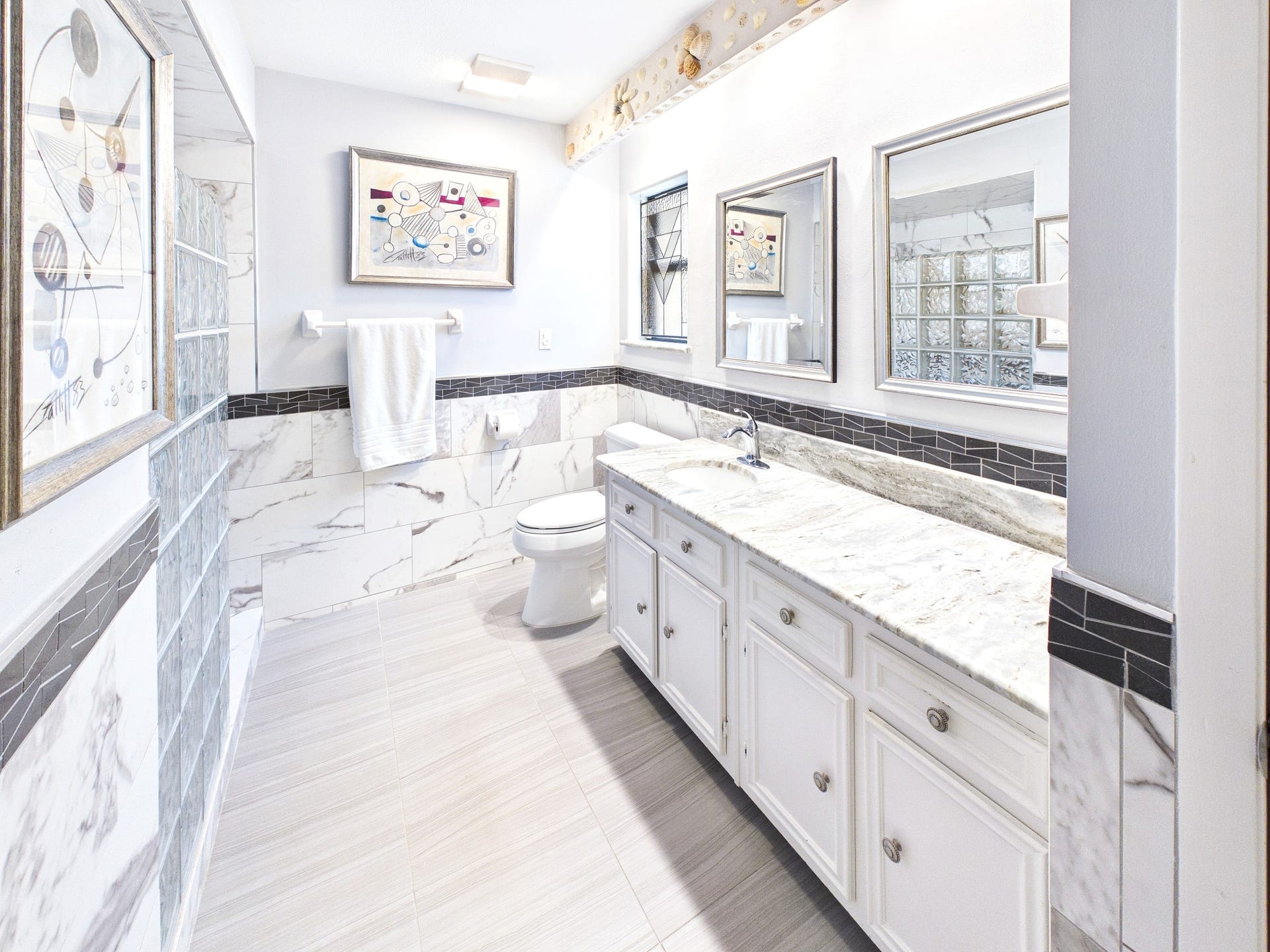 Luxuriate in the serene elegance of this primary bath, featuring a stunning marble-topped double vanity, chic modern tiles, and abundant natural light that elevates your daily routine.