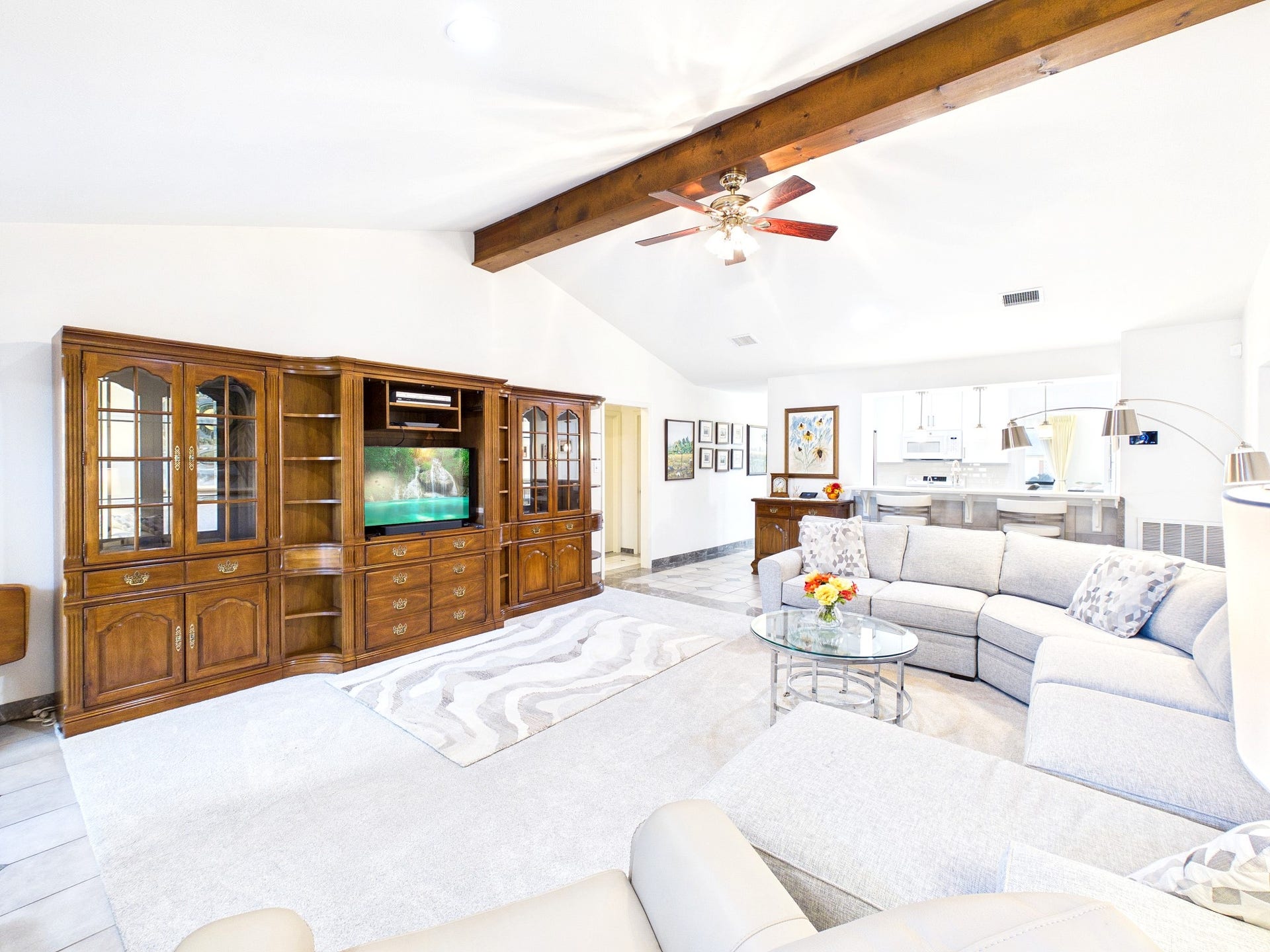Spacious and inviting living area with a vaulted ceiling and exposed beam, ready for your personal touch once the entertainment center is removed, seamlessly flowing into a modern kitchen perfect for gatherings.