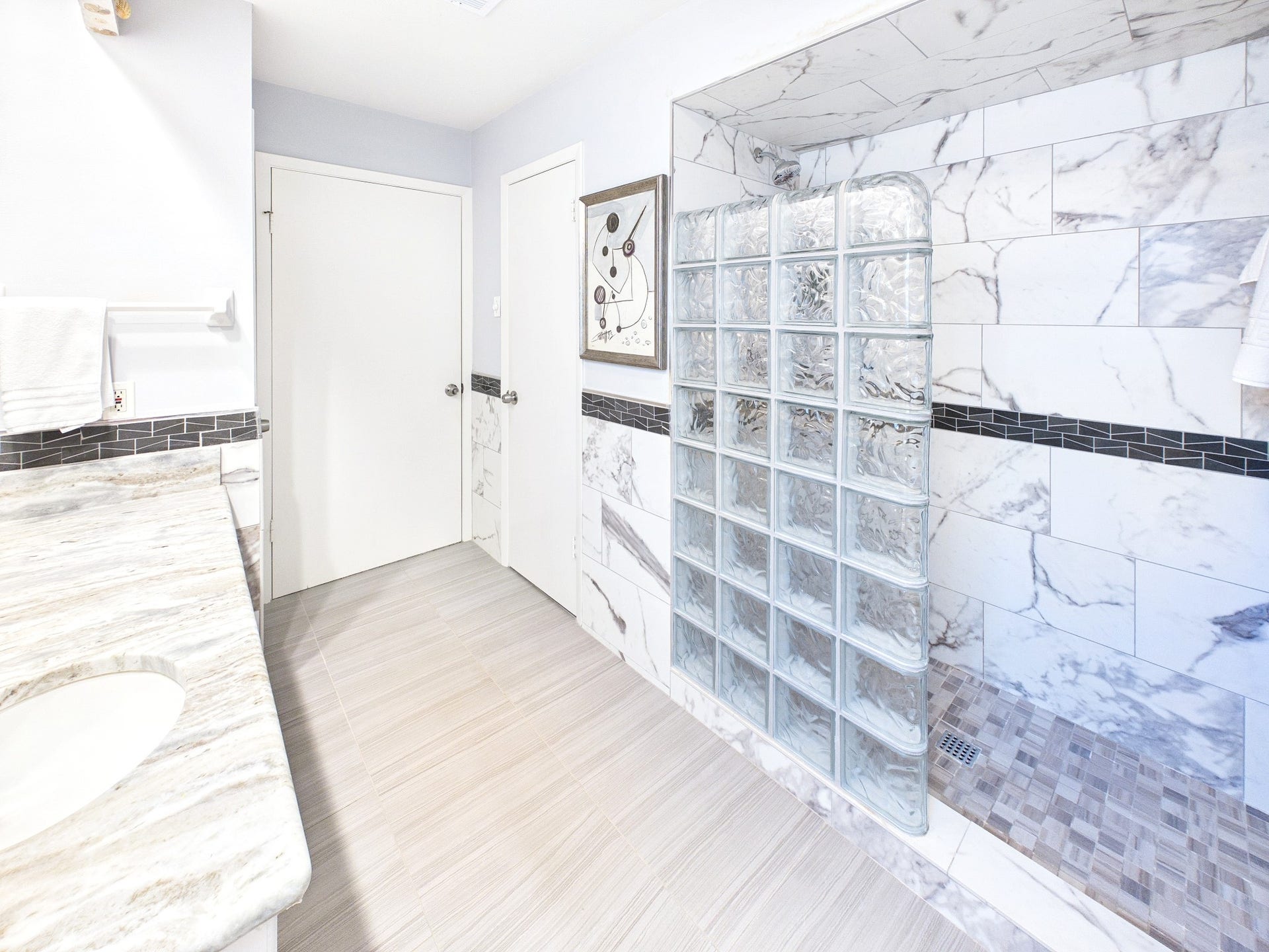 Experience luxury in the primary bath with sleek marble finishes, stylish glass block accents, and modern tile flooring for a spa-like retreat.