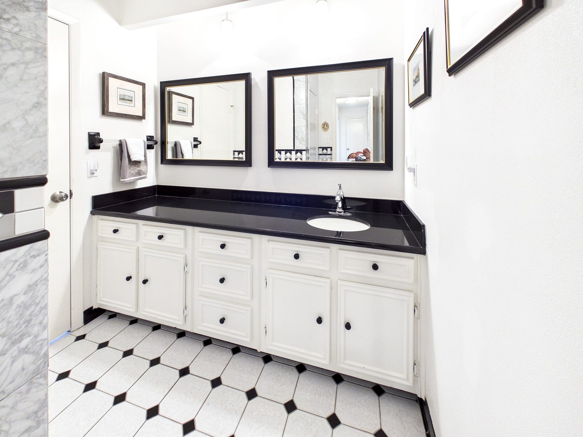 Elegant black and white tiles set the stage for a sophisticated bathroom featuring sleek countertops and ample cabinet space.