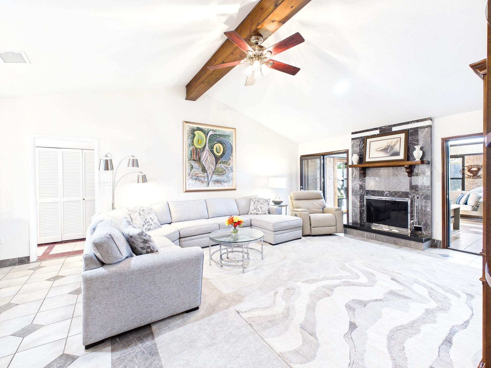 Experience the perfect blend of comfort and elegance in this bright, spacious living room featuring a stylish sectional, cozy fireplace, and vaulted ceiling with exposed beams, ideal for relaxation and entertaining.