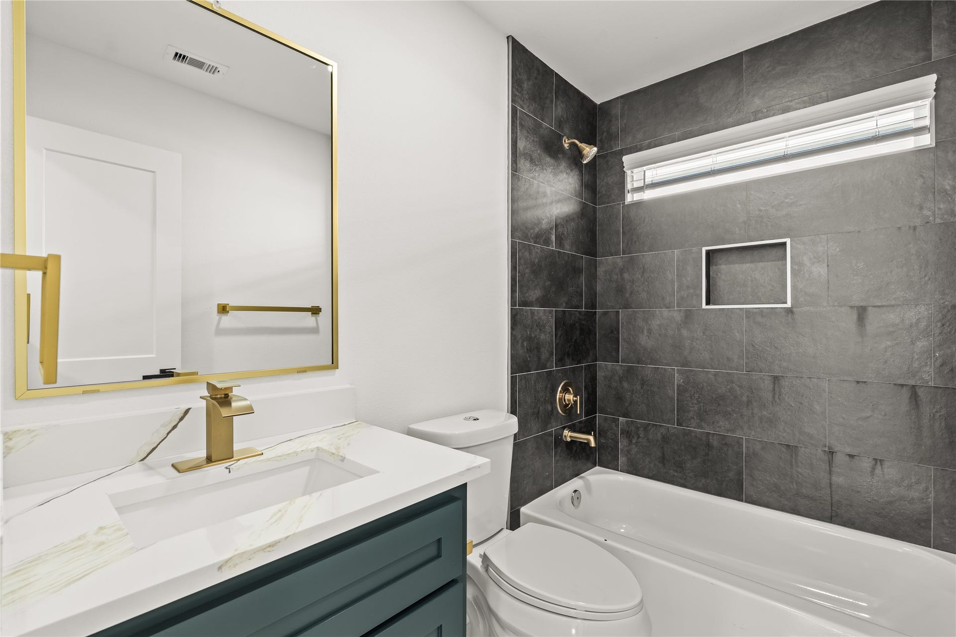 1912 Schweikhardt Street, Houston, TX 77020 Bold, dramatic style. The full upstairs guest bathroom showcases a striking floor-to-ceiling charcoal tile accent wall paired with an elegant emerald vanity and gold hardware.