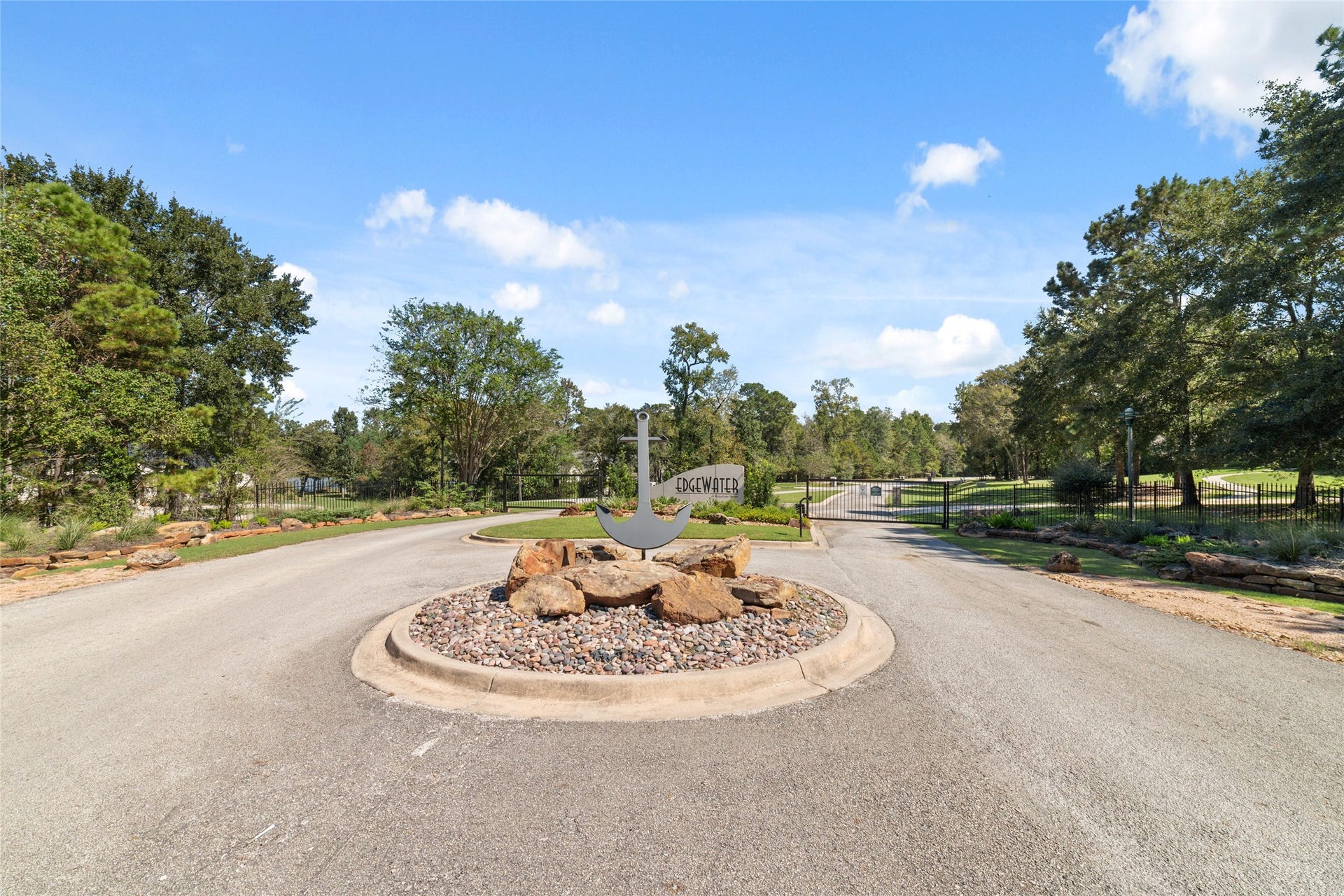 0 Ridgelake Court, Montgomery, TX 77316 Charming gated entrance to Edgewater, featuring a beautifully landscaped roundabout with natural stone accents, surrounded by lush greenery and mature trees.