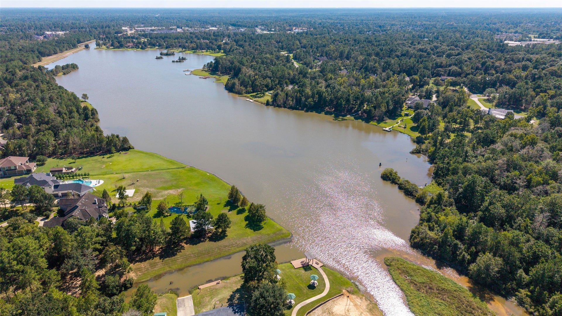 0 Ridgelake Court, Montgomery, TX 77316 Stunning aerial view of a serene lake surrounded by lush greenery and elegant homes, offering a perfect blend of nature and luxury living.