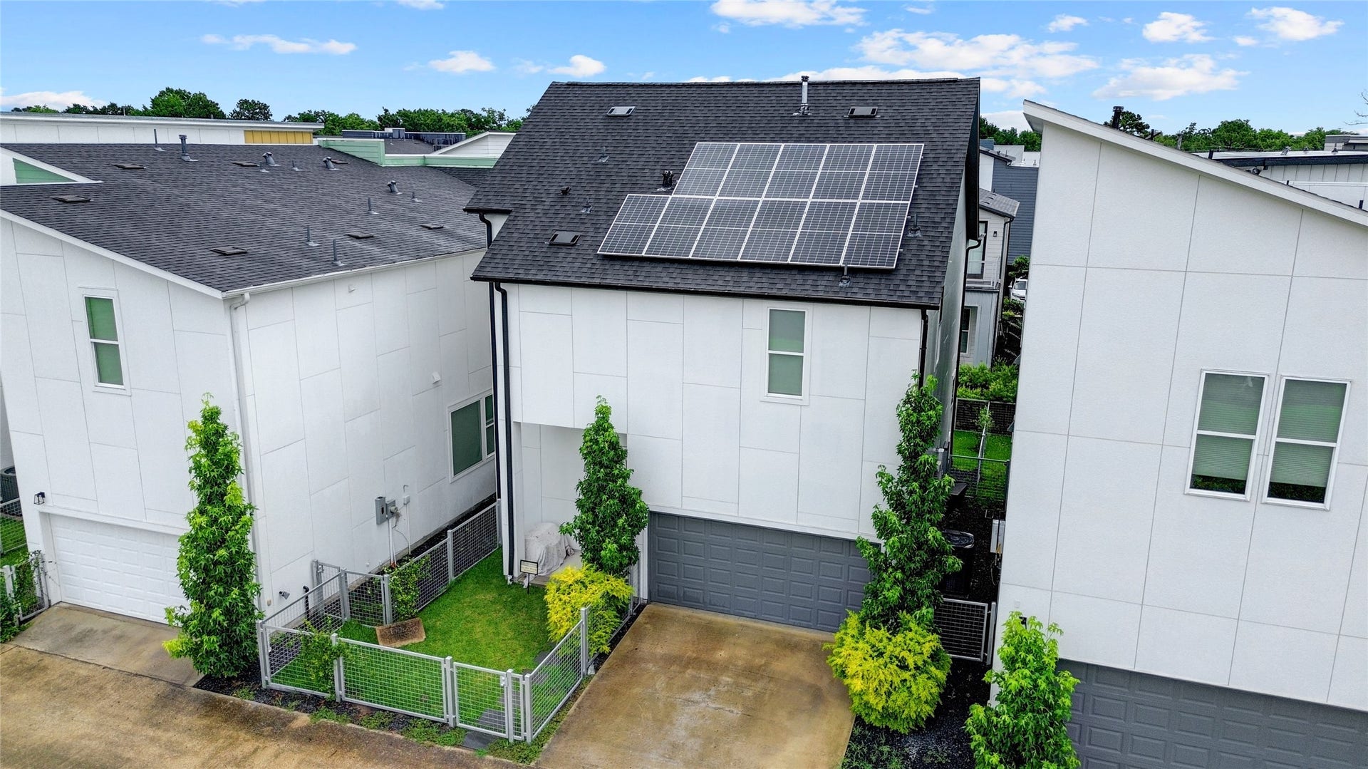 9820 Mocking Bird Hill Lane, Houston, TX 77080 Modern home rear view, with sleek solar panels and a double wide driveway and spacious two-car garage, nestled between lush greenery and a well-maintained fenced yard.