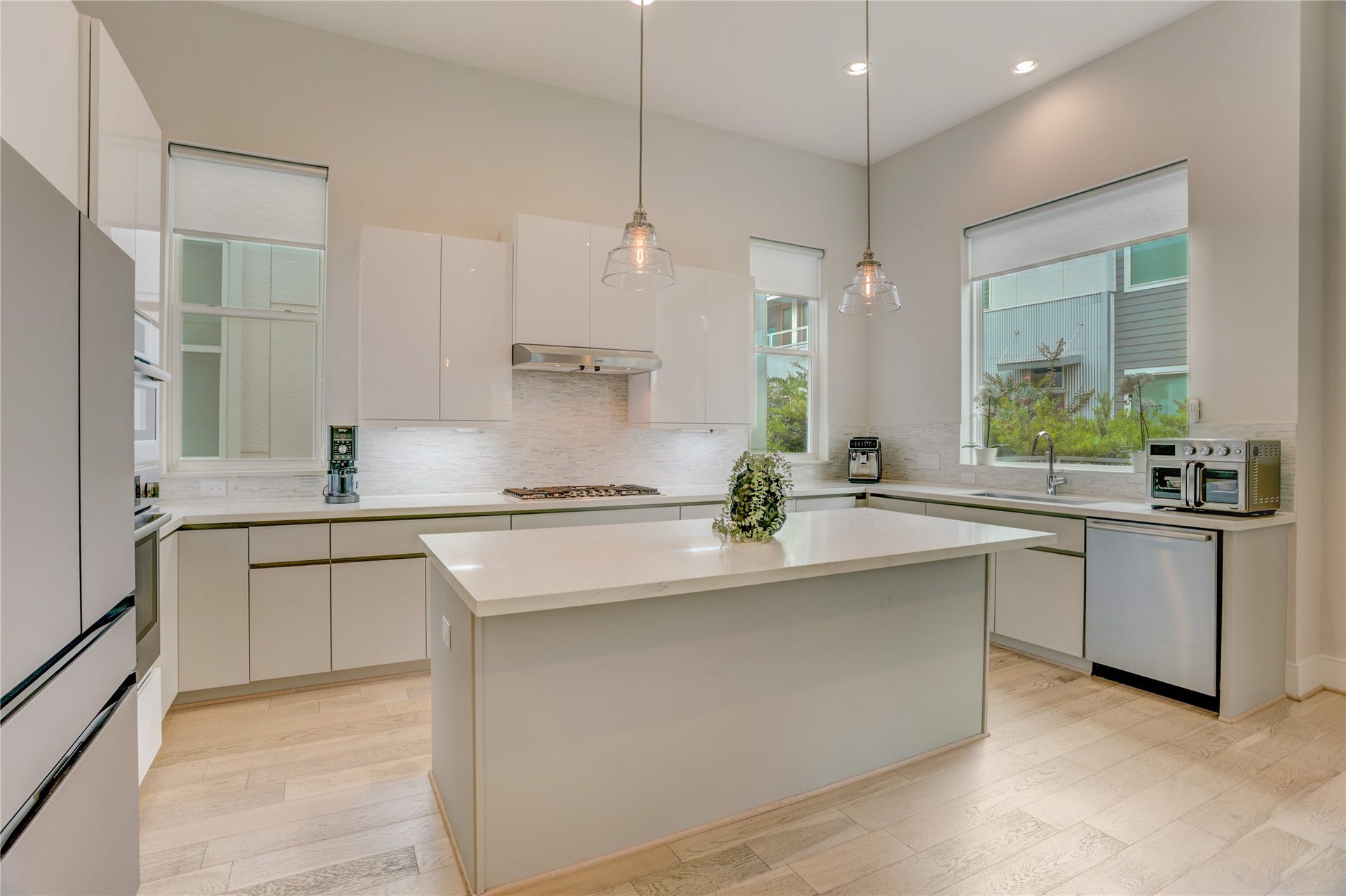 9820 Mocking Bird Hill Lane, Houston, TX 77080 Modern kitchen with sleek white cabinetry, a spacious island, and stainless steel appliances, illuminated by stylish pendant lighting and natural light from large windows.