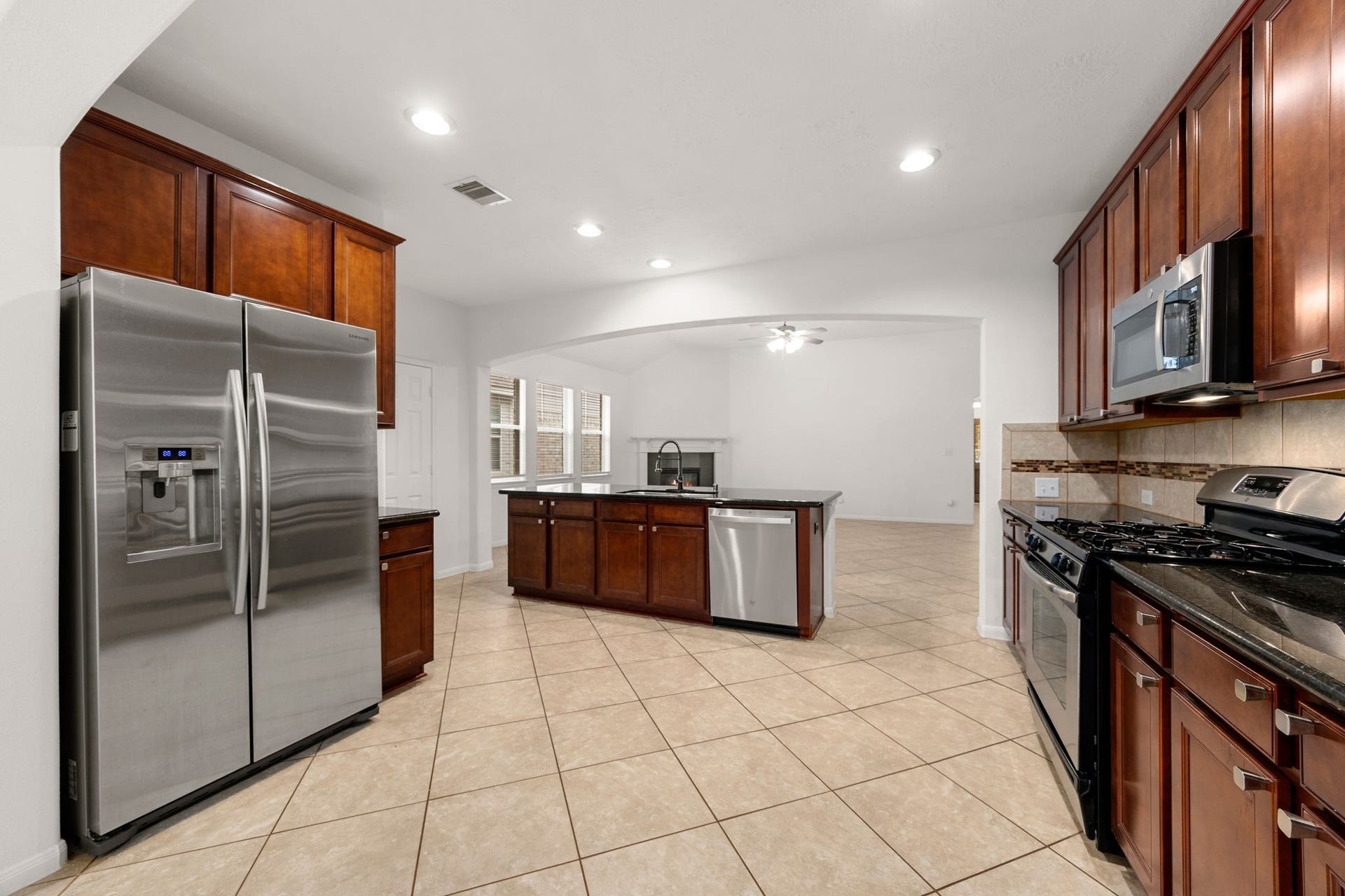26311 Smokey Valley Lane, Katy, TX 77494 Rich cherry-tone cabinetry and stainless steel appliances define the kitchen, including a brand-new dishwasher set into the island, with views straight through to the fireplace.