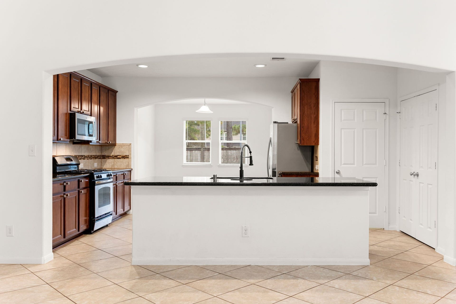 26311 Smokey Valley Lane, Katy, TX 77494 A sweeping arched opening frames the kitchen, where a large granite-topped island with a breakfast bar takes center stage and convenient pantry storage sits just steps away.