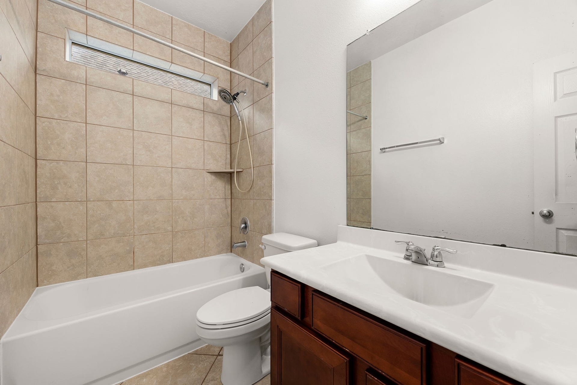 26311 Smokey Valley Lane, Katy, TX 77494 The secondary bathroom features cherry-tone cabinetry, a wide vanity mirror, and a tub/shower combination with a tile surround, a handheld showerhead, and a transom window.