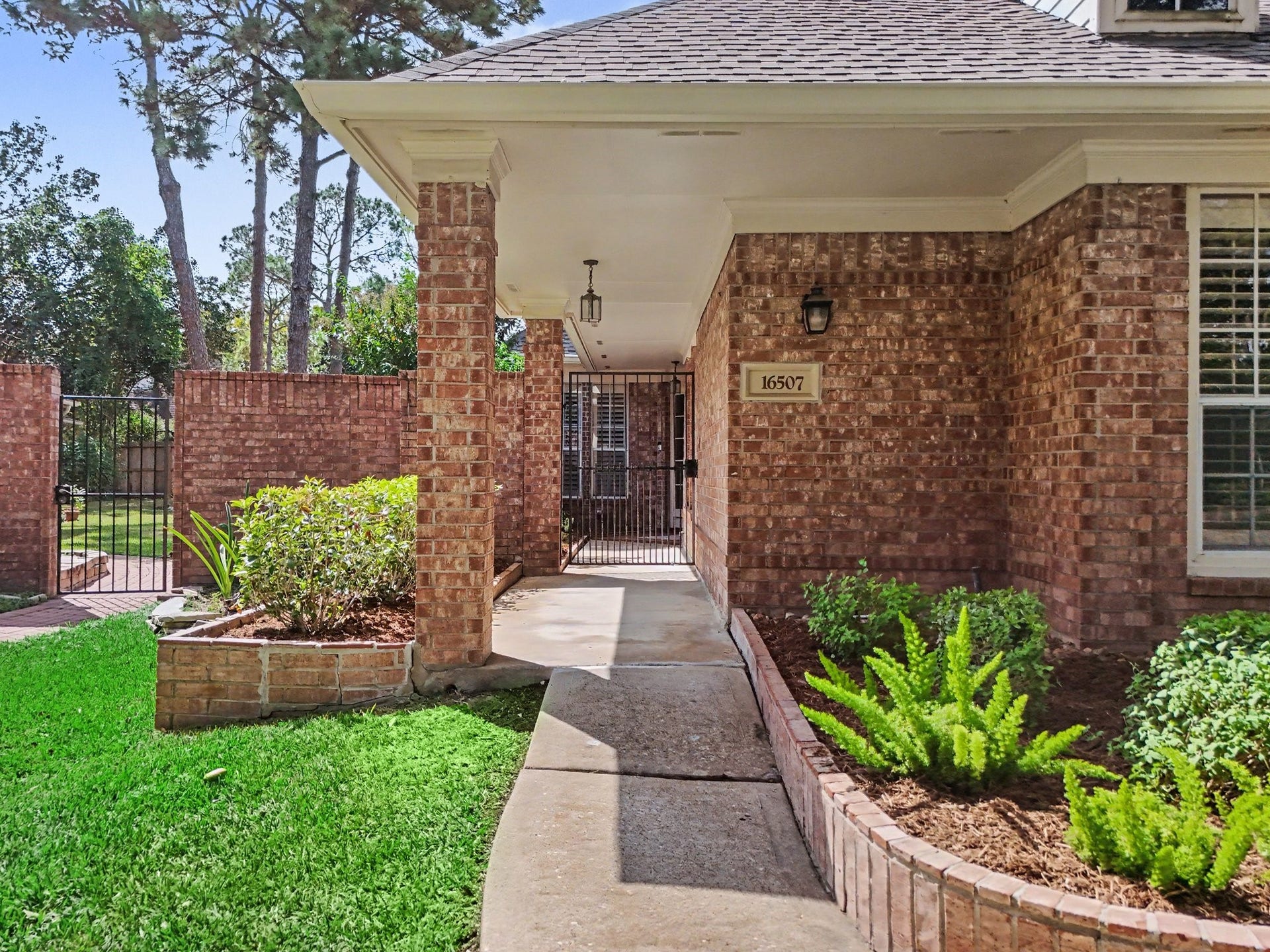 16507 Heather Meadow Court, Pasadena, TX 77059 Covered front entry walkway featuring classic brick detailing, landscaped garden beds, and a welcoming pathway leading to the front door.