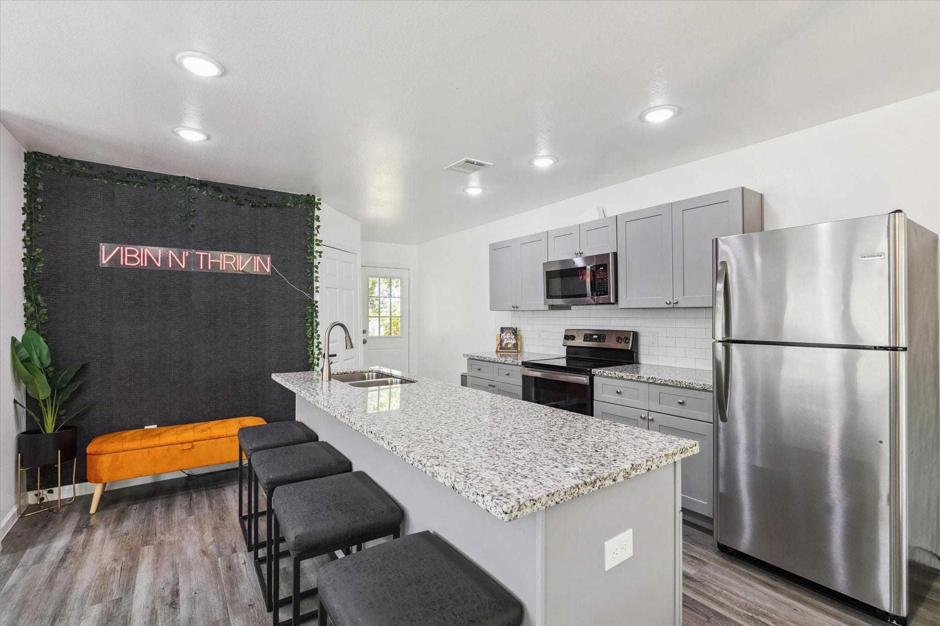 Sleek recessed lighting brightens the kitchen, highlighting granite countertops, subway tile, and stainless steel appliances. The oversized island with bar seating anchors the space, perfect for everyday living or casual gatherings.