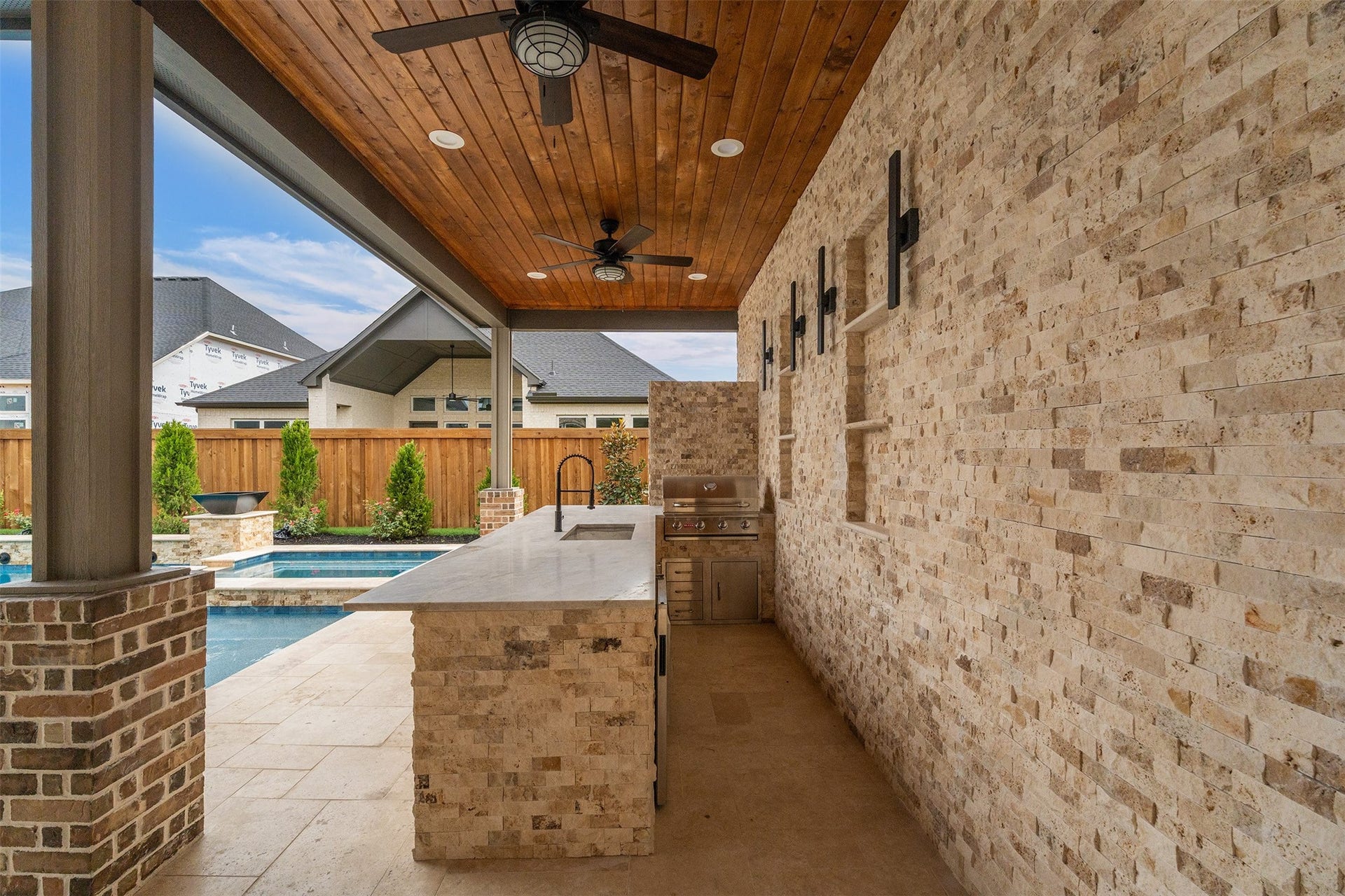 28033 Pebble Park Drive, Spring, TX 77386 Outdoor kitchen with sconce lighting, bead board ceiling, bar seating, fans, sink, grill, fridge and wired for a sauna.
