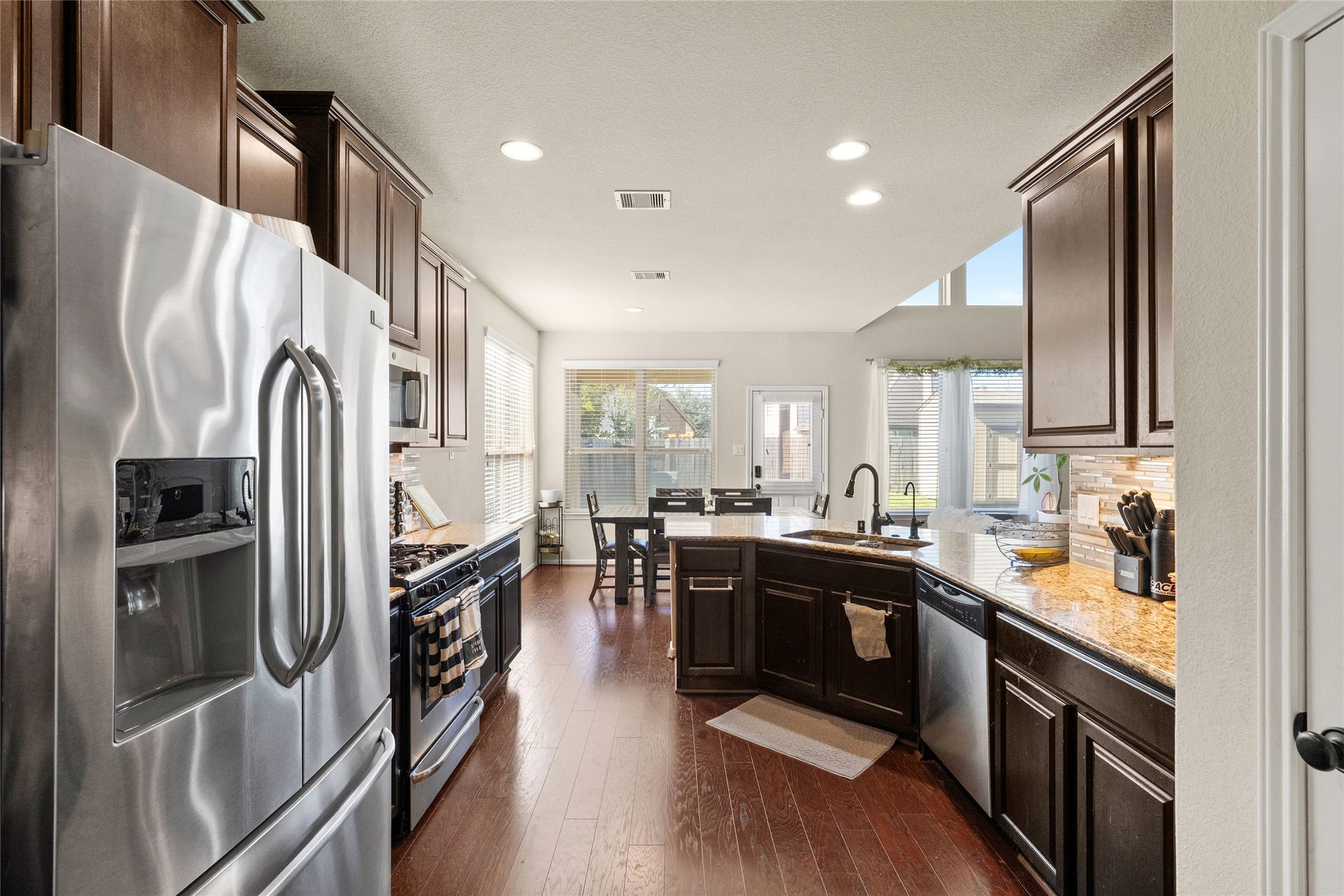 3650 Daintree Park Drive, Katy, TX 77494 Spacious kitchen with rich dark cabinetry, stainless steel appliances, and granite countertops, leading to a bright dining area with large windows and natural light.