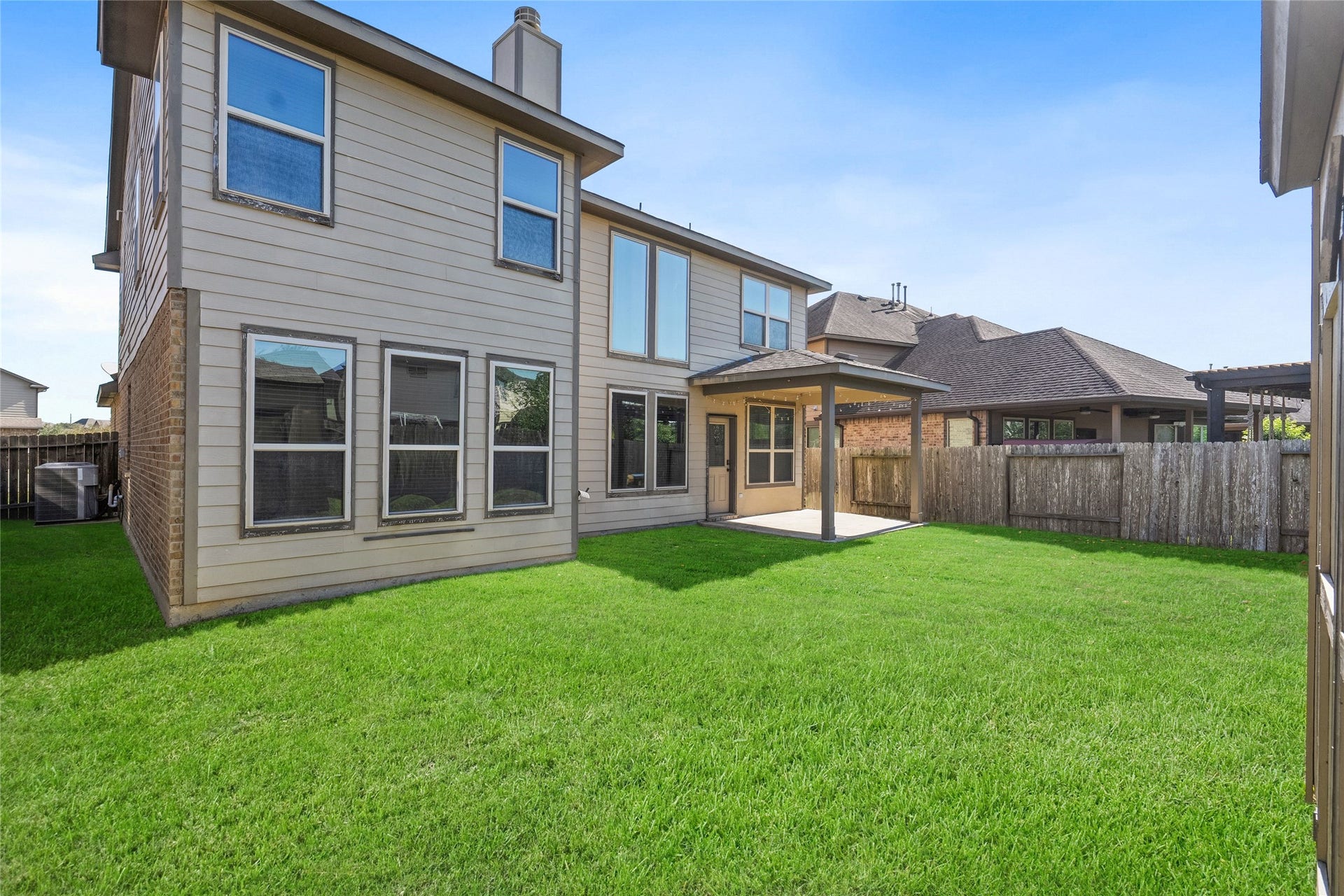 3650 Daintree Park Drive, Katy, TX 77494 Spacious backyard with a well-maintained lawn, featuring a two-story home with large windows and a covered patio, perfect for outdoor relaxation and entertaining.