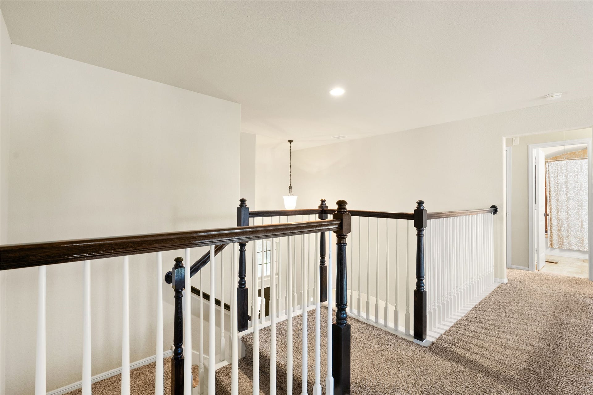3650 Daintree Park Drive, Katy, TX 77494 Bright and airy upstairs landing featuring elegant dark wood railing and plush carpeting, leading to a cozy bedroom and bathroom.