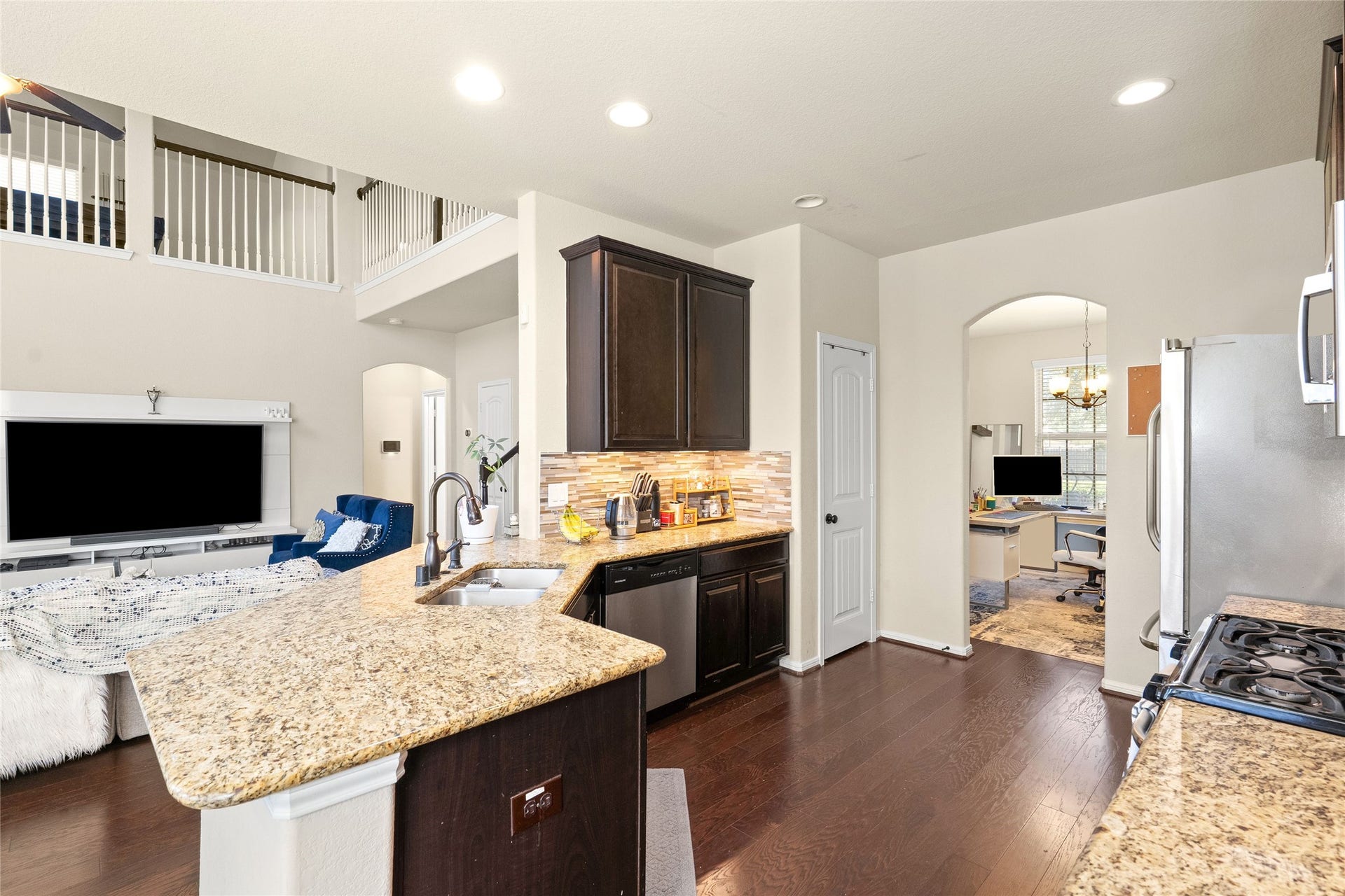 3650 Daintree Park Drive, Katy, TX 77494 Spacious kitchen with elegant granite countertops, dark cabinetry, and stainless steel appliances, seamlessly flowing into a cozy living area with an adjacent home office space.