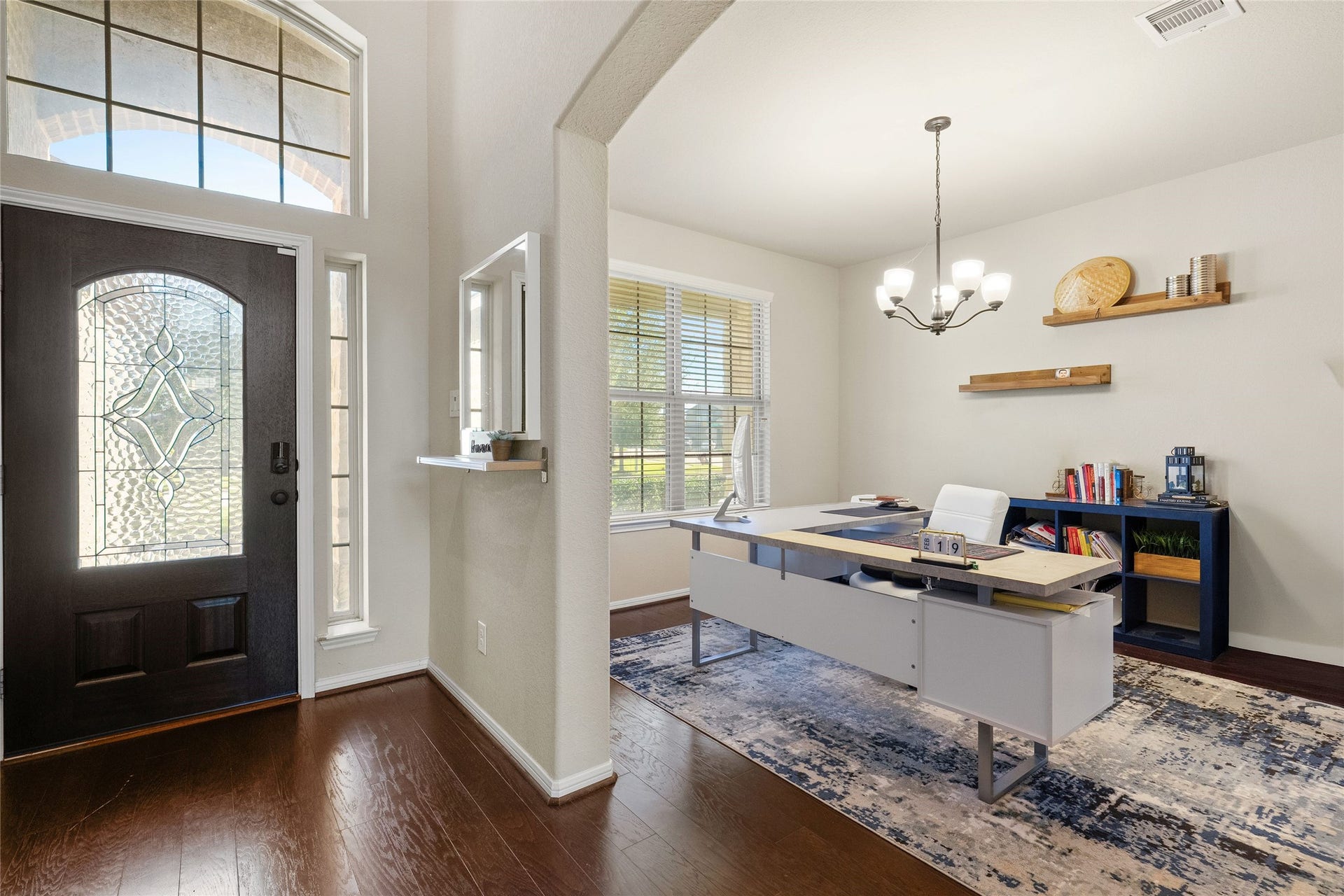 3650 Daintree Park Drive, Katy, TX 77494 Elegant home office with abundant natural light, featuring a modern desk, stylish chandelier, and built-in shelving, adjacent to a welcoming entryway with a decorative glass door.
