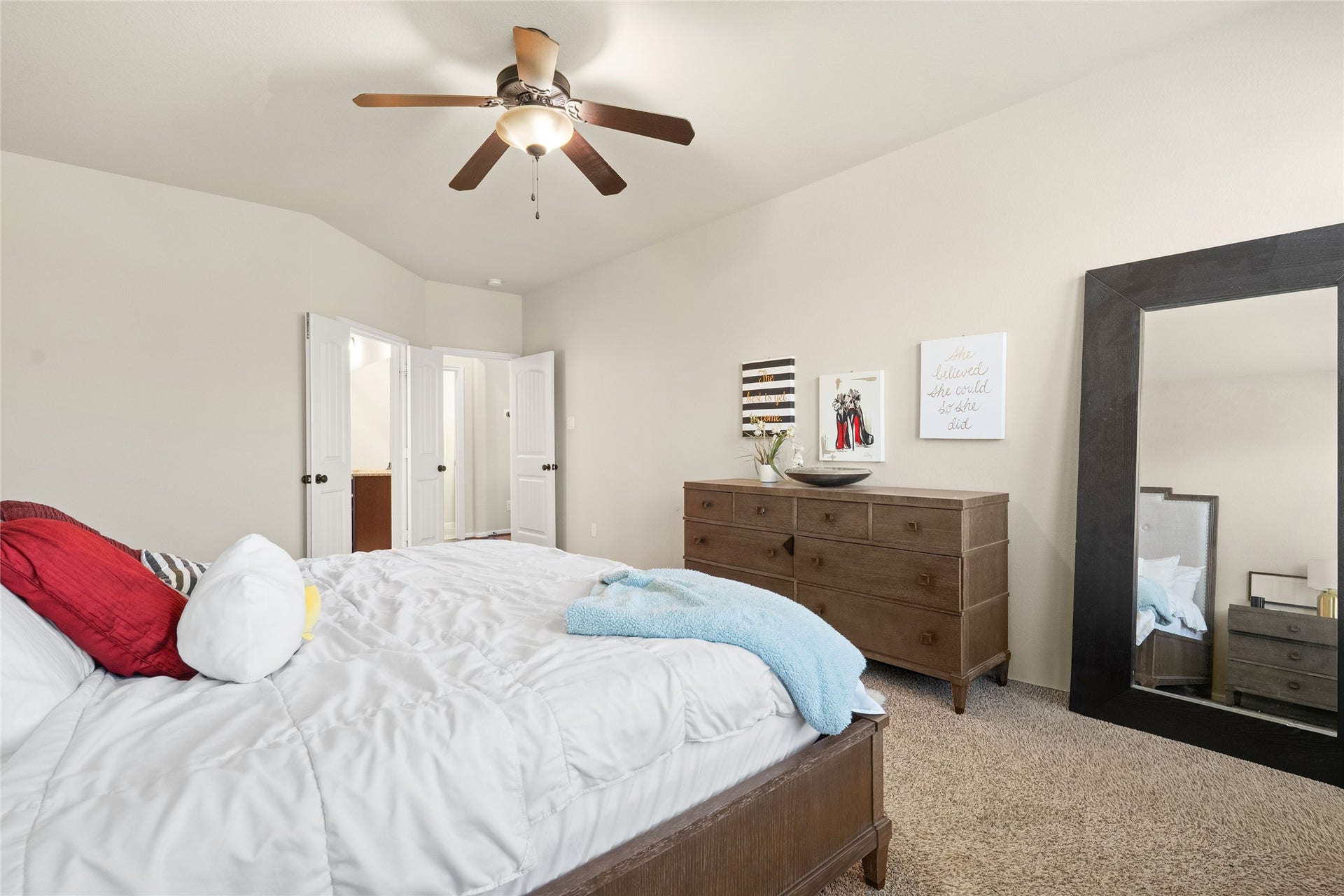 3650 Daintree Park Drive, Katy, TX 77494 Spacious bedroom with plush carpeting, featuring a stylish ceiling fan and ample natural light. The room includes a large mirror, elegant dresser, and inviting double doors leading to an en-suite area.