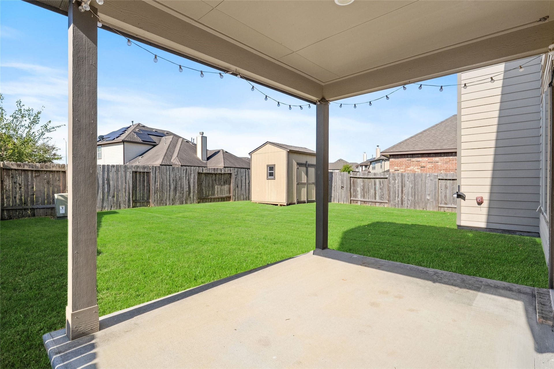 3650 Daintree Park Drive, Katy, TX 77494 Spacious backyard featuring a covered patio with string lights, perfect for outdoor gatherings, and a large storage shed for added convenience.