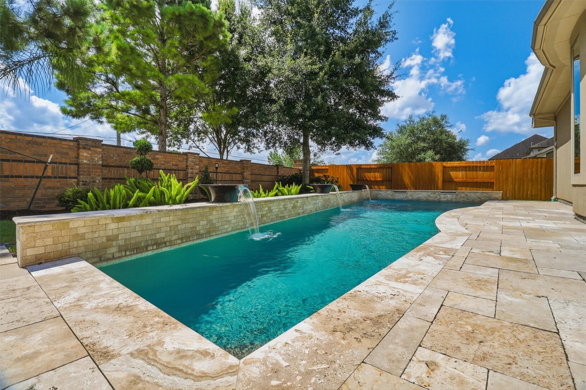Gorgeous travertine decking surrounds the classic pool with three water bowl features and two shears at the far end of the pool. This is a low maintenance yard, yet still provides plenty of spaces for relaxing and entertaining!