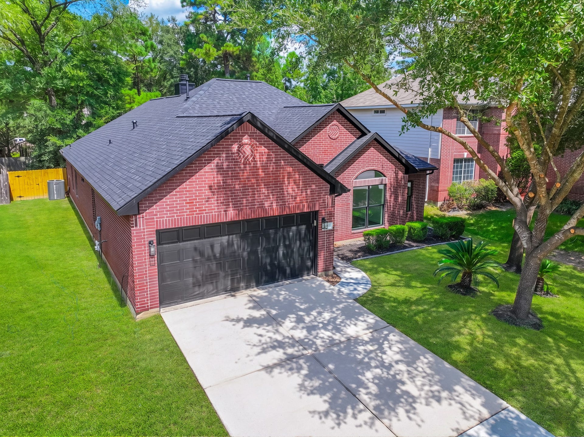 18 Griffin Hill Court, The Woodlands, TX 77382 A different perspective of 18 Griffin Hill Court's charming exterior reveals the home's generous proportions and well-maintained brick construction. The lush green lawn, manicured landscaping, and attached two-car garage are visible from this angle, showcasing the property's excellent curb appeal and pride of ownership.