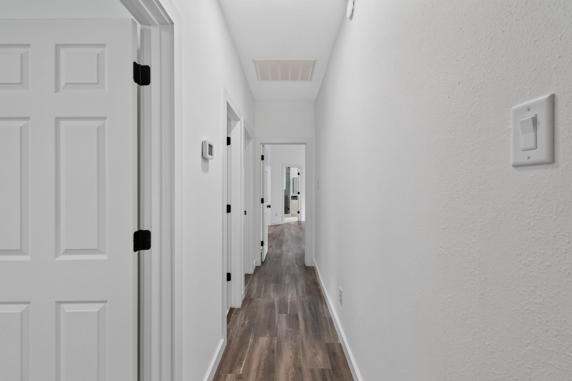 18 Griffin Hill Court, The Woodlands, TX 77382 The hallway at 18 Griffin Hill Court connects the home's private bedroom wing with clean architectural lines and easy accessibility. Pristine white walls and dark hardwood-style flooring create a bright, cohesive corridor that flows naturally between rooms a reflection of the home's thoughtful design and meticulous attention to functional detail.