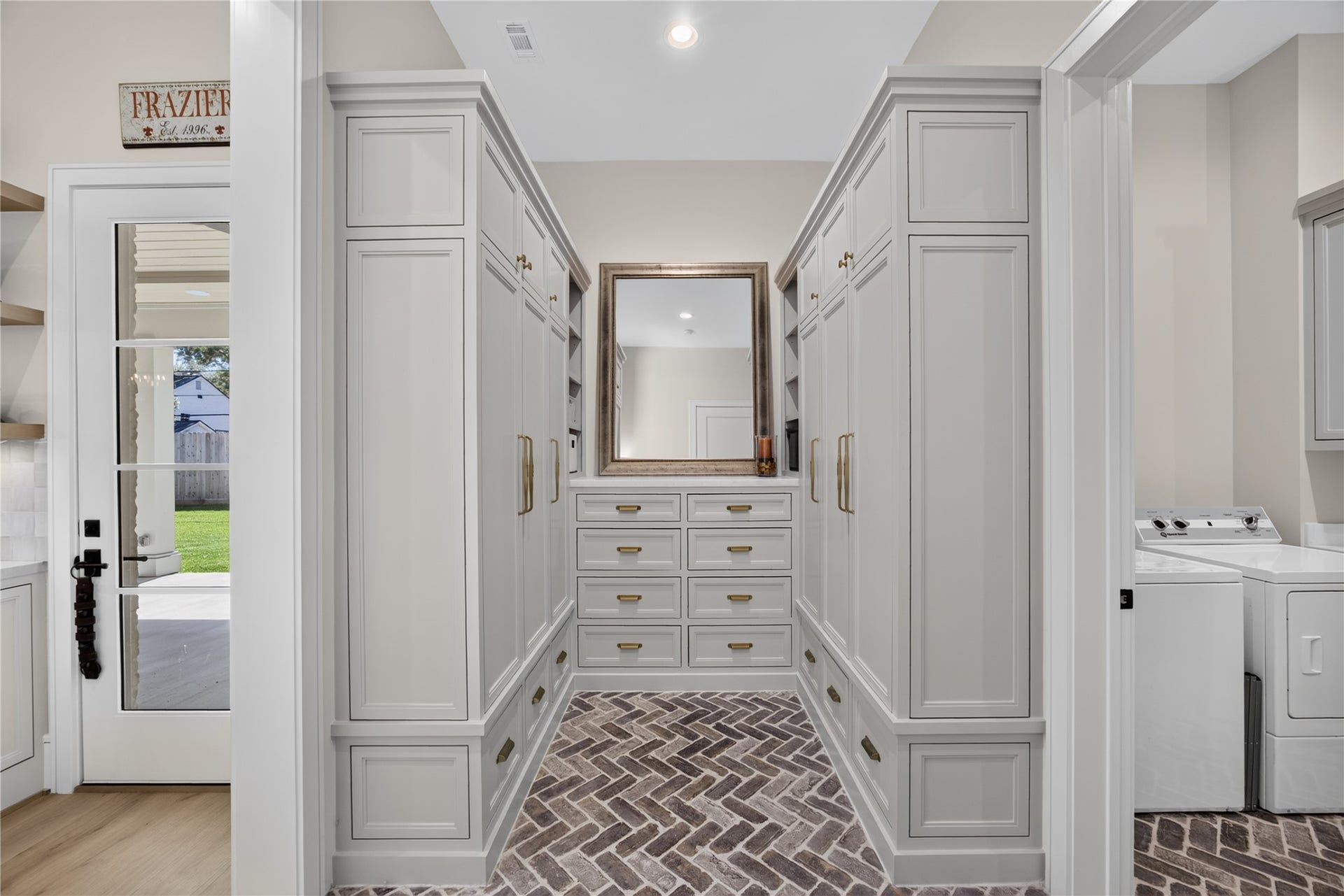 13915 Queensbury Lane, Houston, TX 77079 A beautifully designed mudroom featuring floor-to-ceiling custom cabinetry, abundant storage, elegant gold hardware, and distinctive herringbone brick flooring. Conveniently located near the backyard access and downstairs laundry room, this functional space provides an organized transition for everyday living.