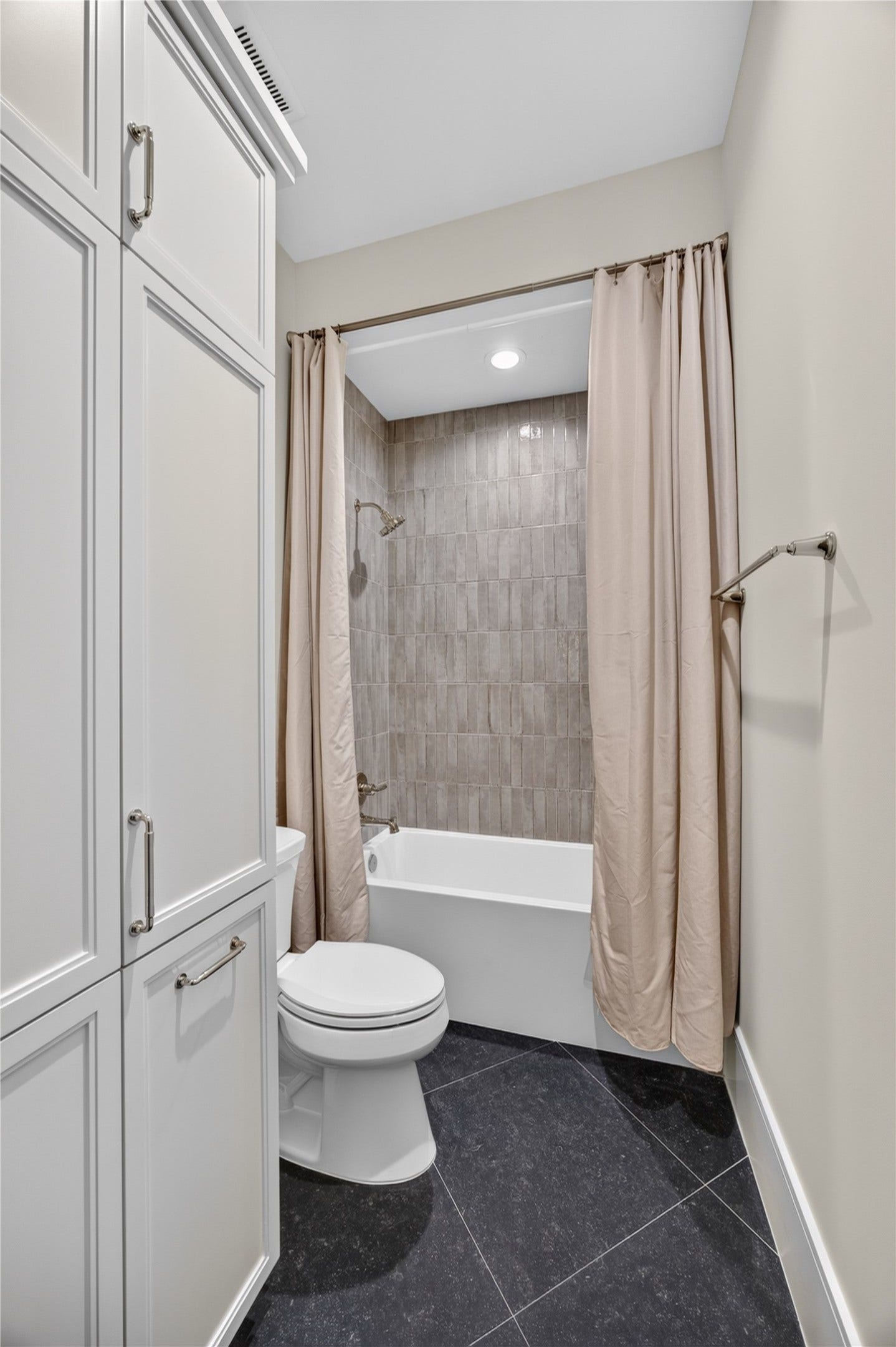 13915 Queensbury Lane, Houston, TX 77079 Additional view of the secondary bathroom highlighting the tub and shower combination with floor-to-ceiling tile surround, built-in storage cabinetry, and contrasting dark tile flooring. A practical and thoughtfully finished space with plenty of storage.