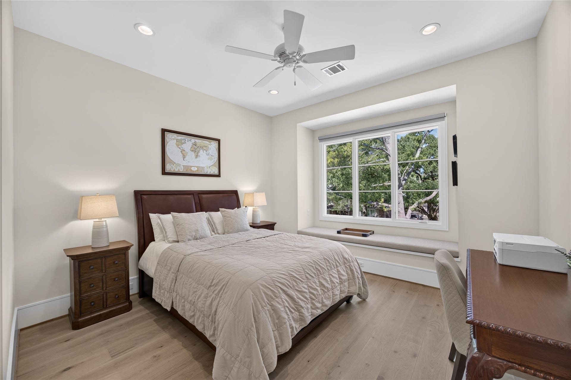 13915 Queensbury Lane, Houston, TX 77079 Bright and inviting secondary bedroom featuring wide-plank wood flooring, recessed lighting, and a spacious window overlooking mature trees. A built-in window seat with storage below creates a charming reading nook, while the generous layout accommodates bedroom furniture and a workspace.