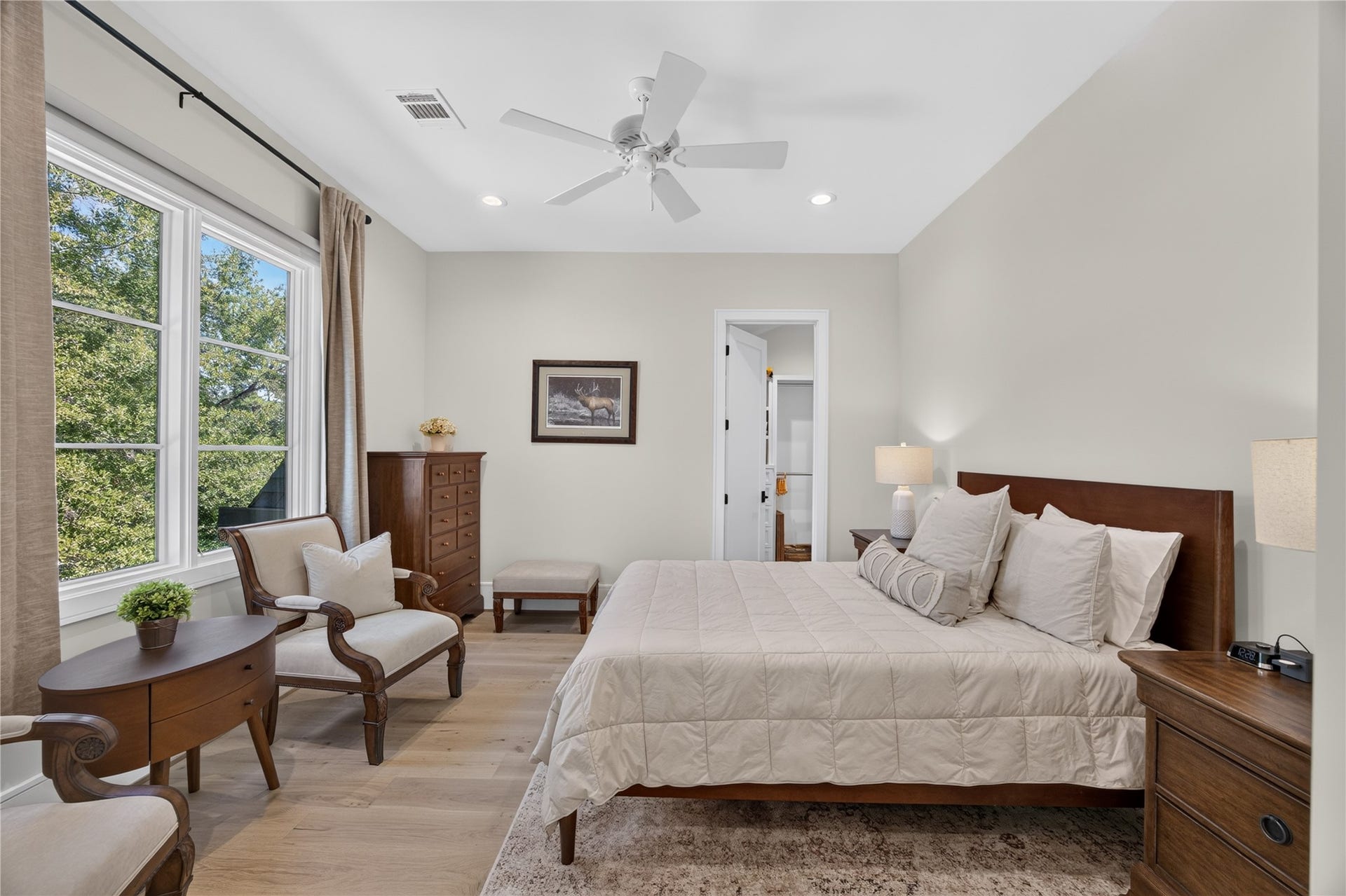 13915 Queensbury Lane, Houston, TX 77079 Spacious secondary bedroom offering beautiful tree-lined views through oversized windows, wide-plank wood flooring, recessed lighting, and a ceiling fan. The generous layout provides flexibility for a comfortable bedroom arrangement with additional seating or a reading area.