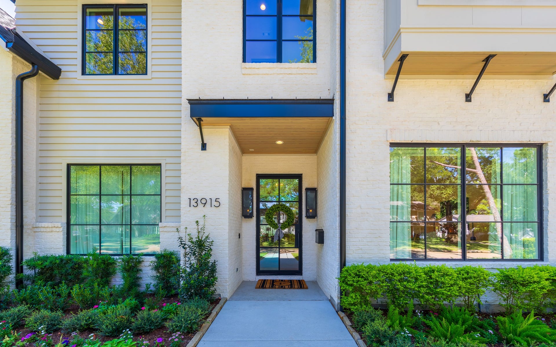 13915 Queensbury Lane, Houston, TX 77079 A welcoming covered entry features warm wood ceiling accents, contemporary black metal detailing, and an elegant glass front door. Oversized windows, exterior sconces, and thoughtfully designed landscaping add character and sophistication to the home's entrance.