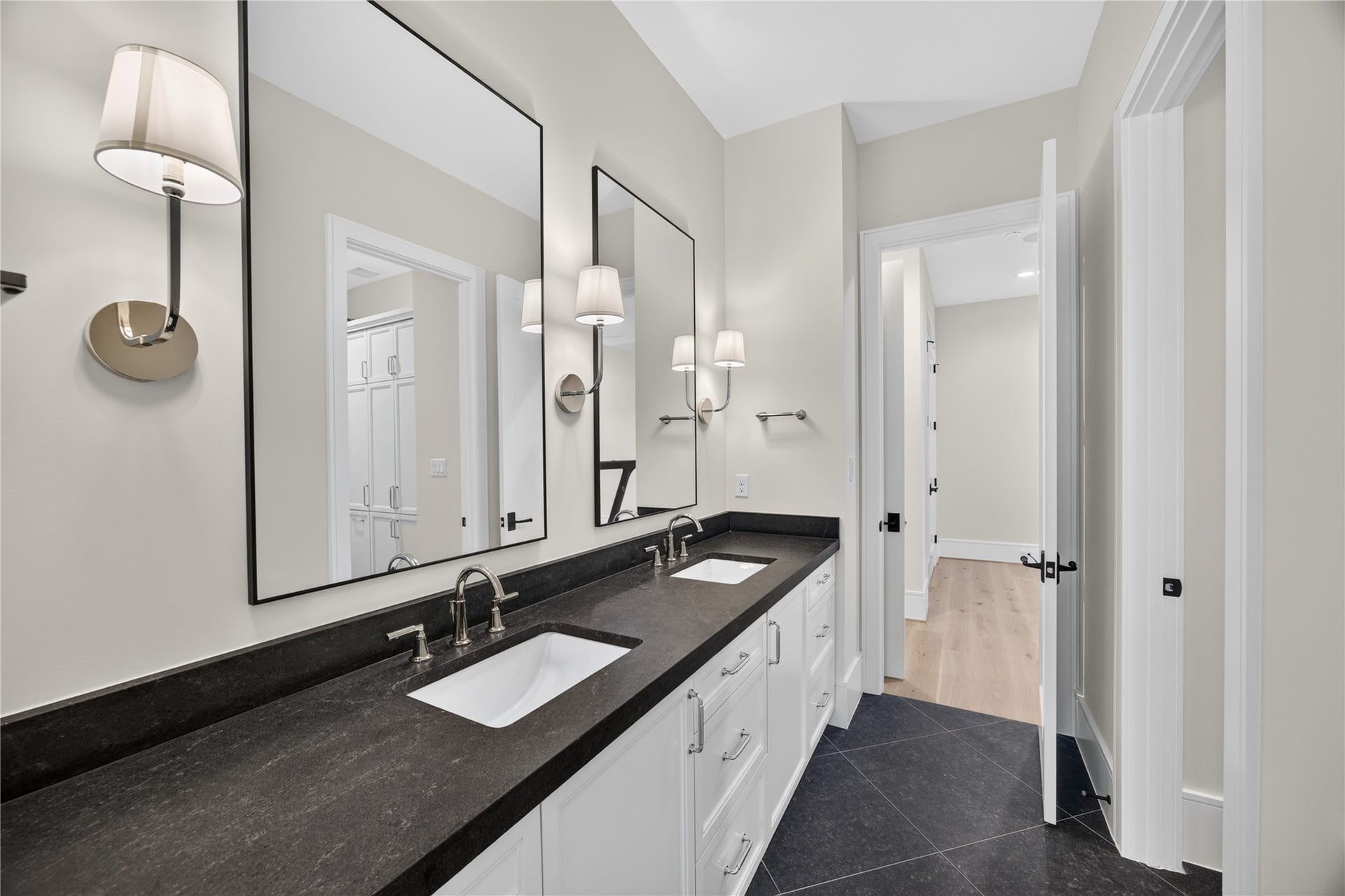 13915 Queensbury Lane, Houston, TX 77079 Well-appointed secondary bathroom featuring a spacious double-sink vanity, dark stone countertops, custom white cabinetry, oversized framed mirrors, and individual wall sconces. The sleek finishes and generous counter space provide both style and functionality.