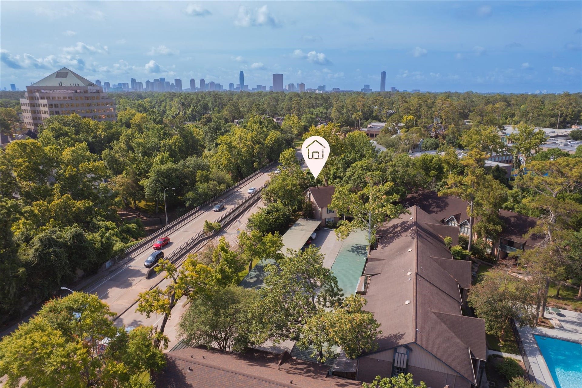 8223 Kingsbrook Road, #212, Houston, TX 77024 This aerial photo showcases a property nestled among lush trees, offering a serene environment. Its conveniently located near a main road and features proximity to urban amenities, with a view of the city skyline in the distance.