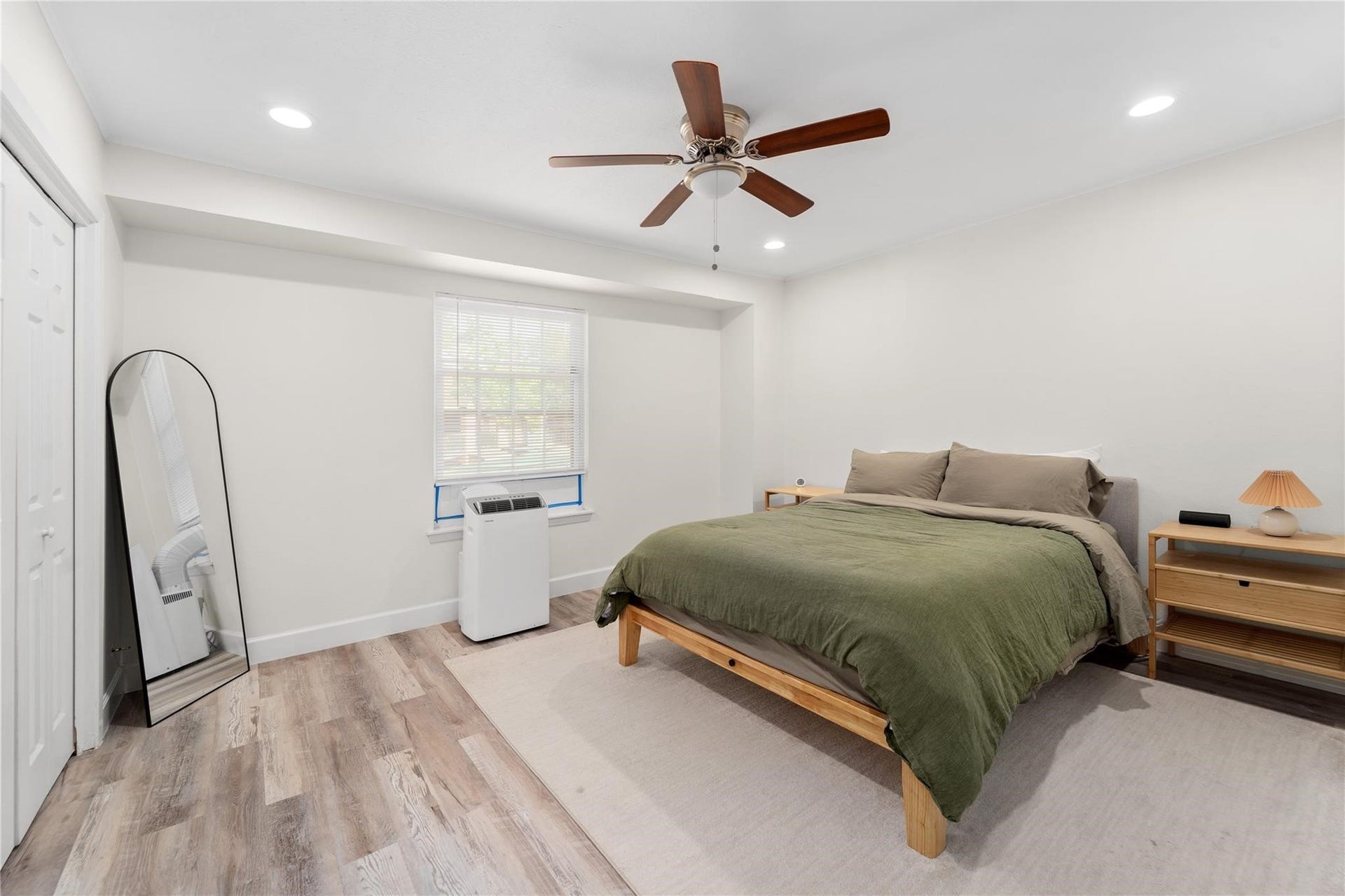 8223 Kingsbrook Road, #212, Houston, TX 77024 This bedroom features a neutral color palette with a cozy bed, modern ceiling fan, and wood-style flooring. It includes a full-length mirror, ample natural light from a window, and minimalist furniture, creating an inviting and serene atmosphere.