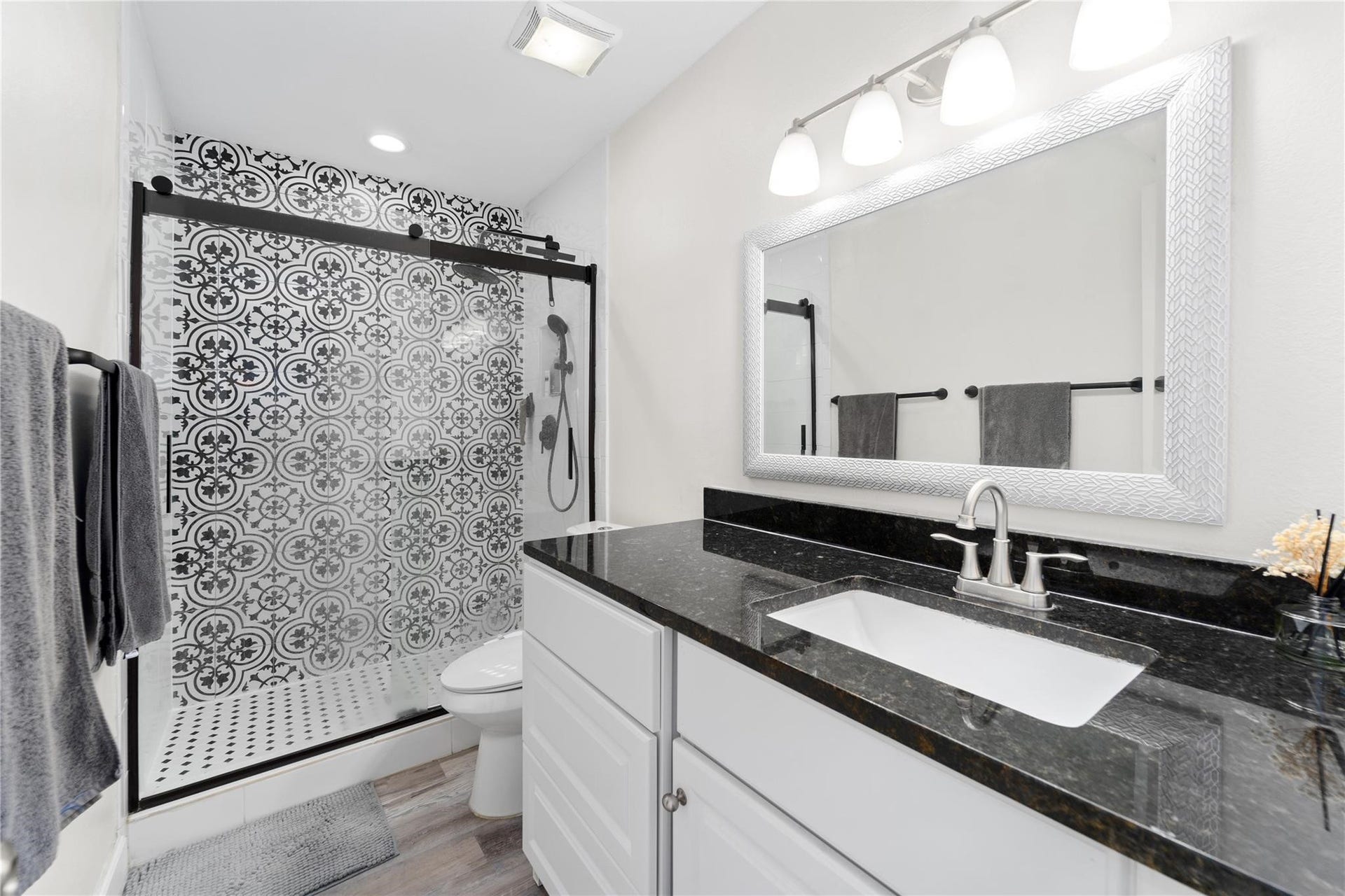 8223 Kingsbrook Road, #212, Houston, TX 77024 This modern bathroom features a stylish black and white patterned shower, a sleek black countertop, and a large mirror with elegant lighting. The space is bright and functional, offering a contemporary feel.