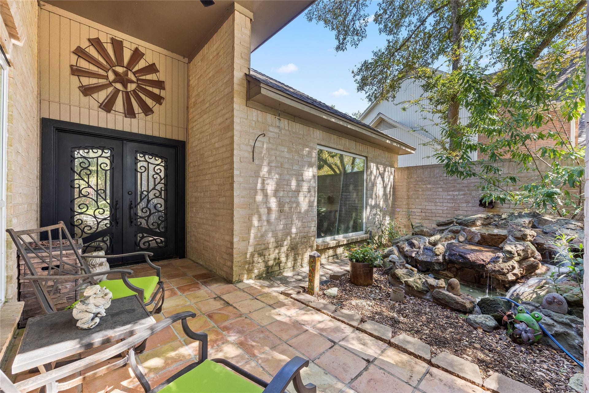1622 Rambling Stone Drive, Richmond, TX 77406 An inviting courtyard features a stone-paved patio, decorative water feature, and striking double entry doors with ornamental ironwork. A charming space to welcome guests or enjoy a quiet moment outdoors.