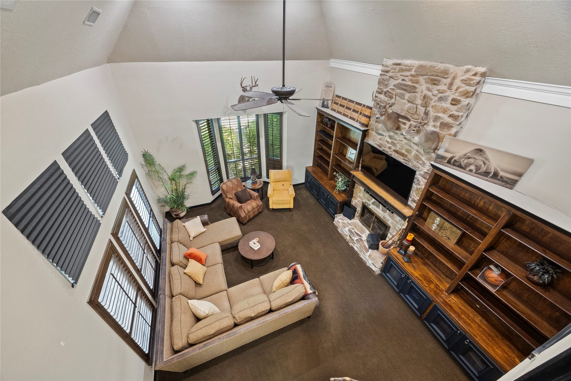 1622 Rambling Stone Drive, Richmond, TX 77406 Overhead view of the two-story living room showcases the dramatic ceiling height, floor-to-ceiling stone fireplace, custom built-ins, and expansive windows. The open design creates a connection between the upstairs game room and main living area below.