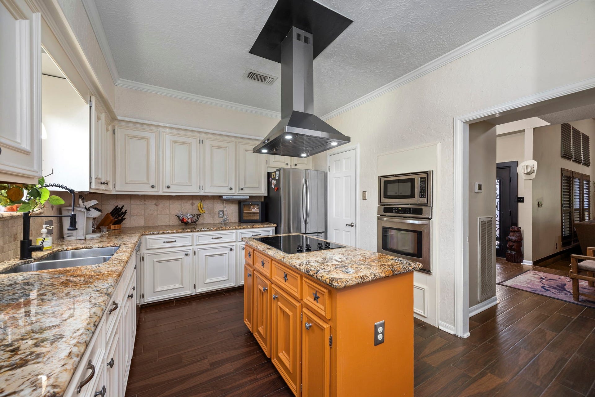 1622 Rambling Stone Drive, Richmond, TX 77406 The kitchen features white cabinetry, granite countertops, a contrasting wood island with cooktop and contemporary vent hood, stainless steel appliances, and built-in double ovens. An open doorway provides convenient access to the main living area.