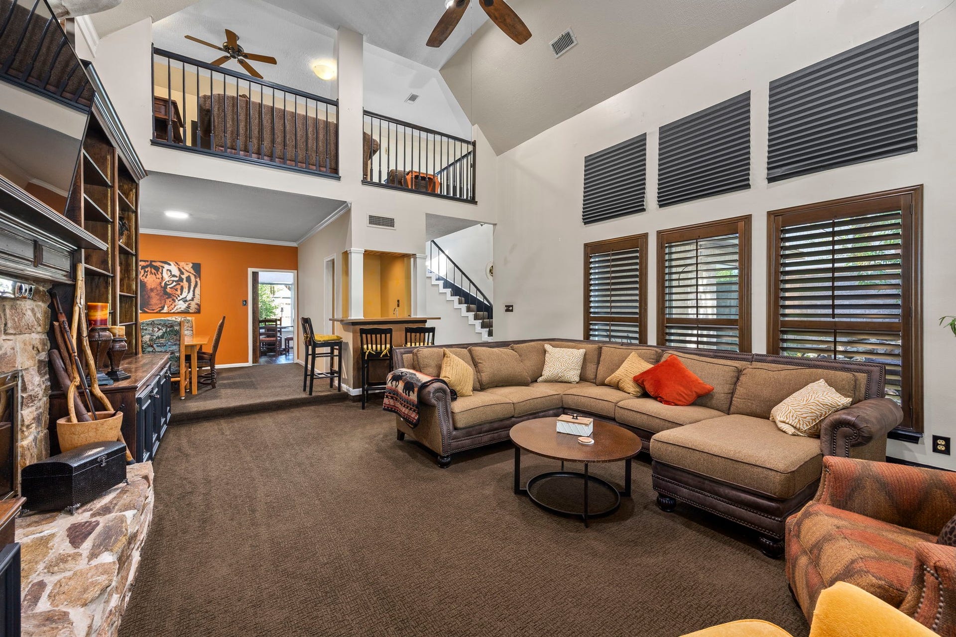 1622 Rambling Stone Drive, Richmond, TX 77406 This perspective showcases the living room's impressive scale, with a wall of windows fitted with plantation shutters, an open balcony above, and convenient access to the adjoining dining area and staircase.