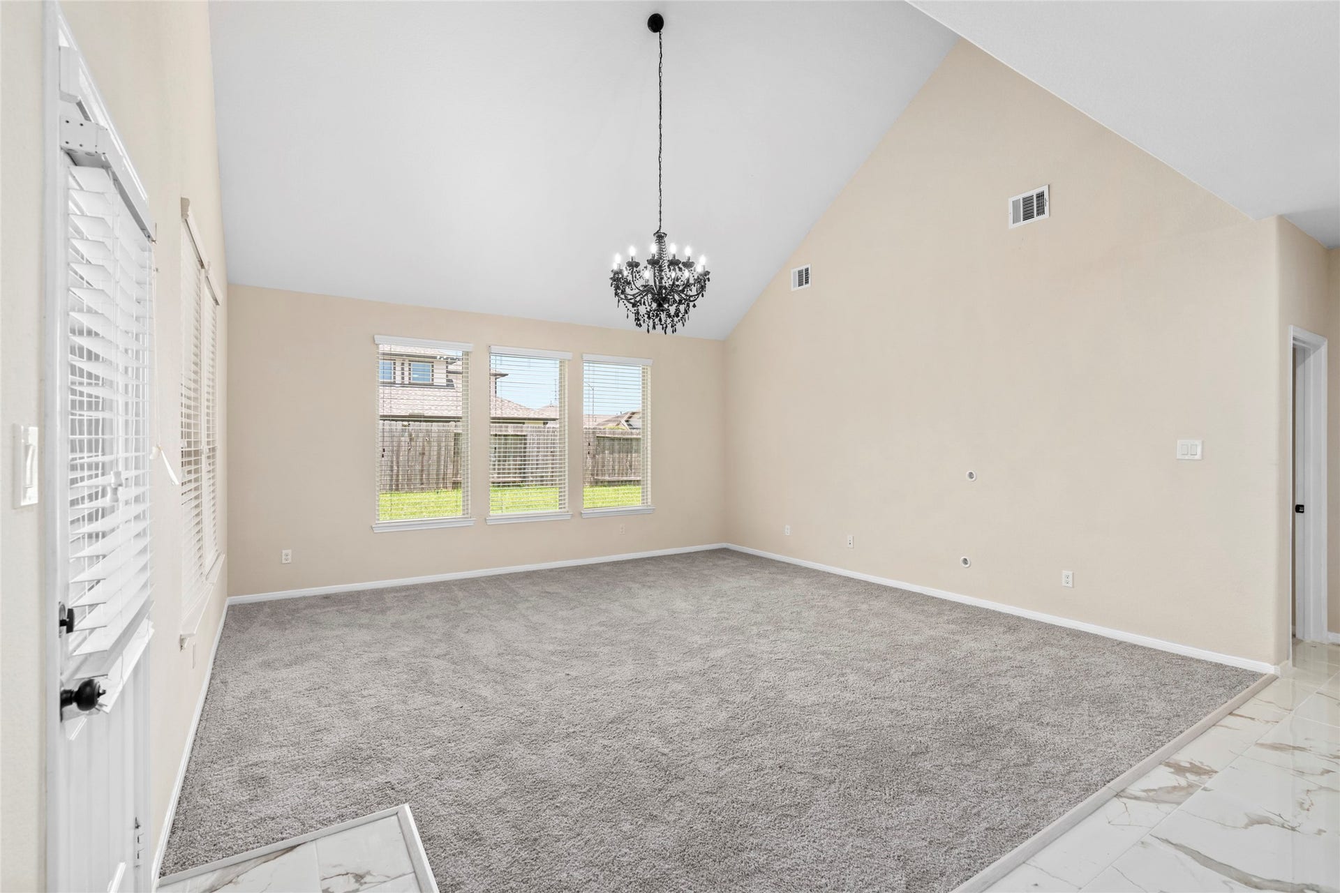 9423 Mineral Rock Lane, Richmond, TX 77407 Bright and inviting, this living room boasts high vaulted ceilings, ample natural light from large windows, and a stunning chandelier, creating a perfect blend of elegance and comfort.